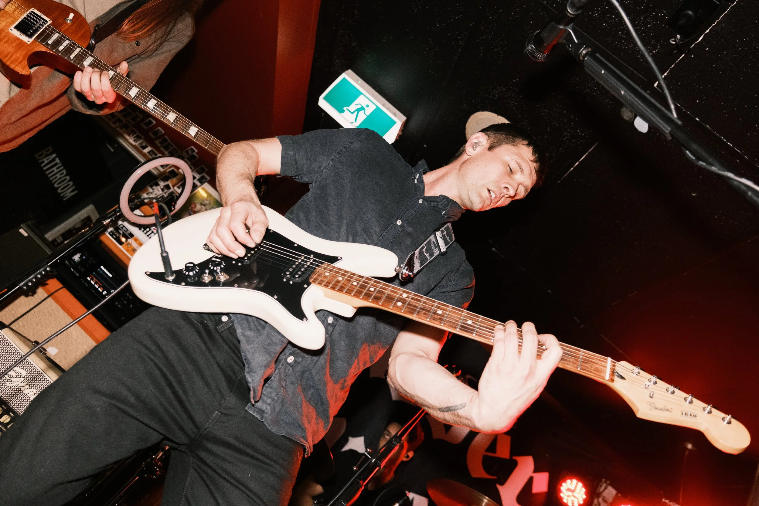 A musician playing an electric guitar on stage with stage lights and sound equipment around him.