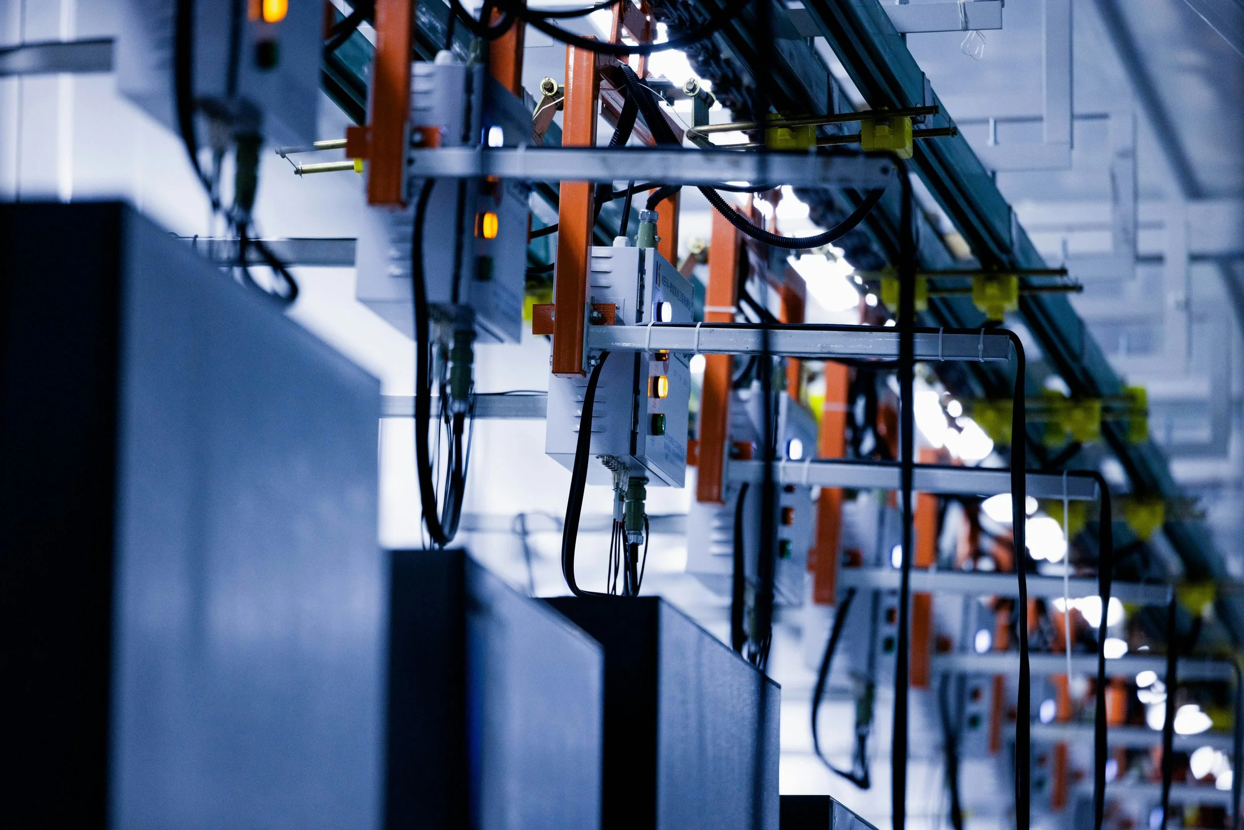 Industrial server room with rows of engaging electronic equipment, cables, and control boxes mounted on a metal rack structure.