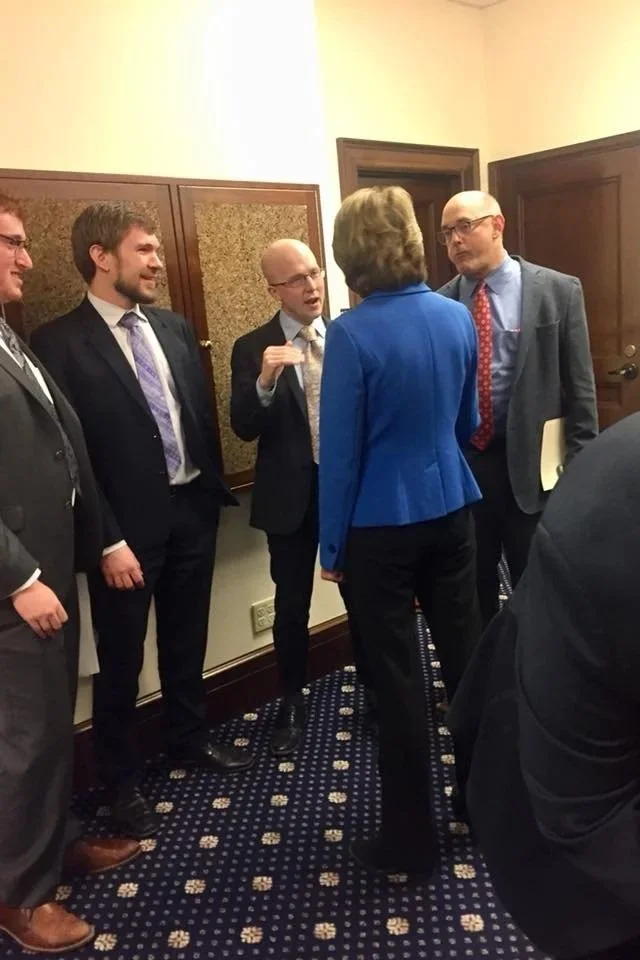 JKT engaged in conversation as an Alaska State Legislator, in a formal setting, dressed in business attire.