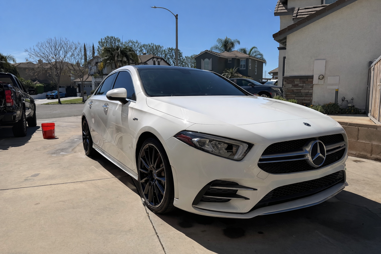 A white Mercedes-Benz sedan parked in a residential driveway on a sunny day.