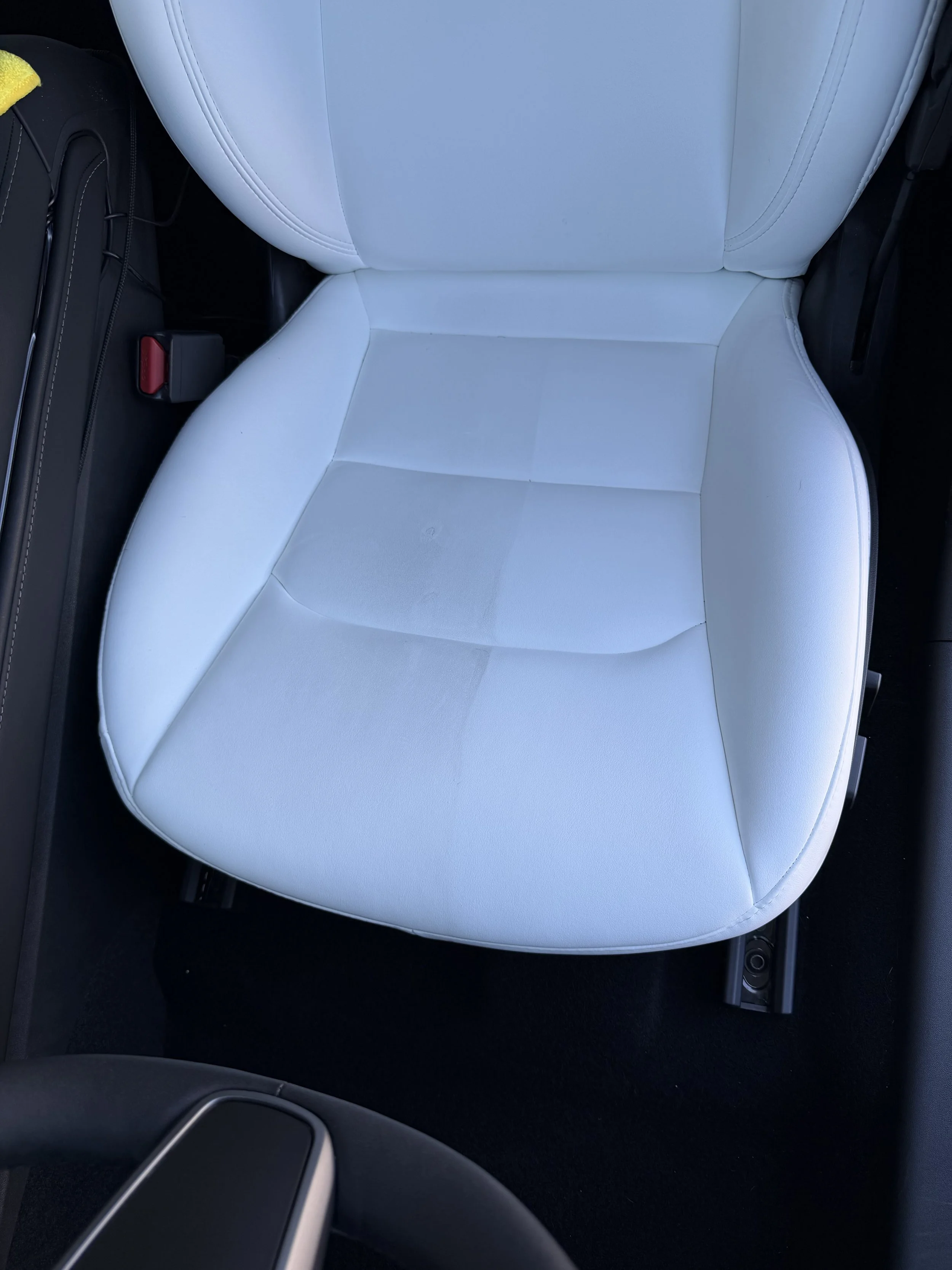 Car interior showing white leather seat, center console with cupholder, and black flooring.