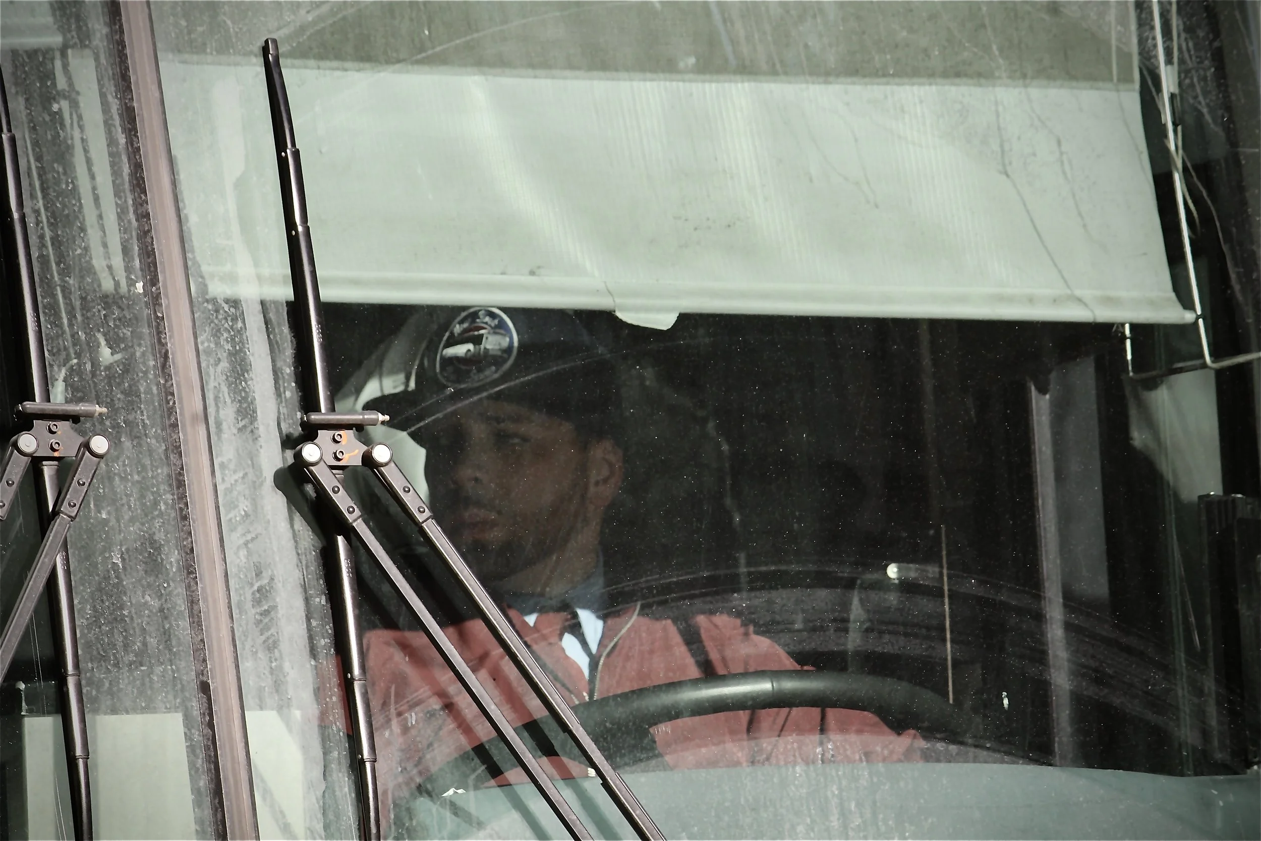 Close-up view through a vehicle windshield showing windshield wipers, a rearview mirror, and a person wearing a red jacket inside the vehicle.