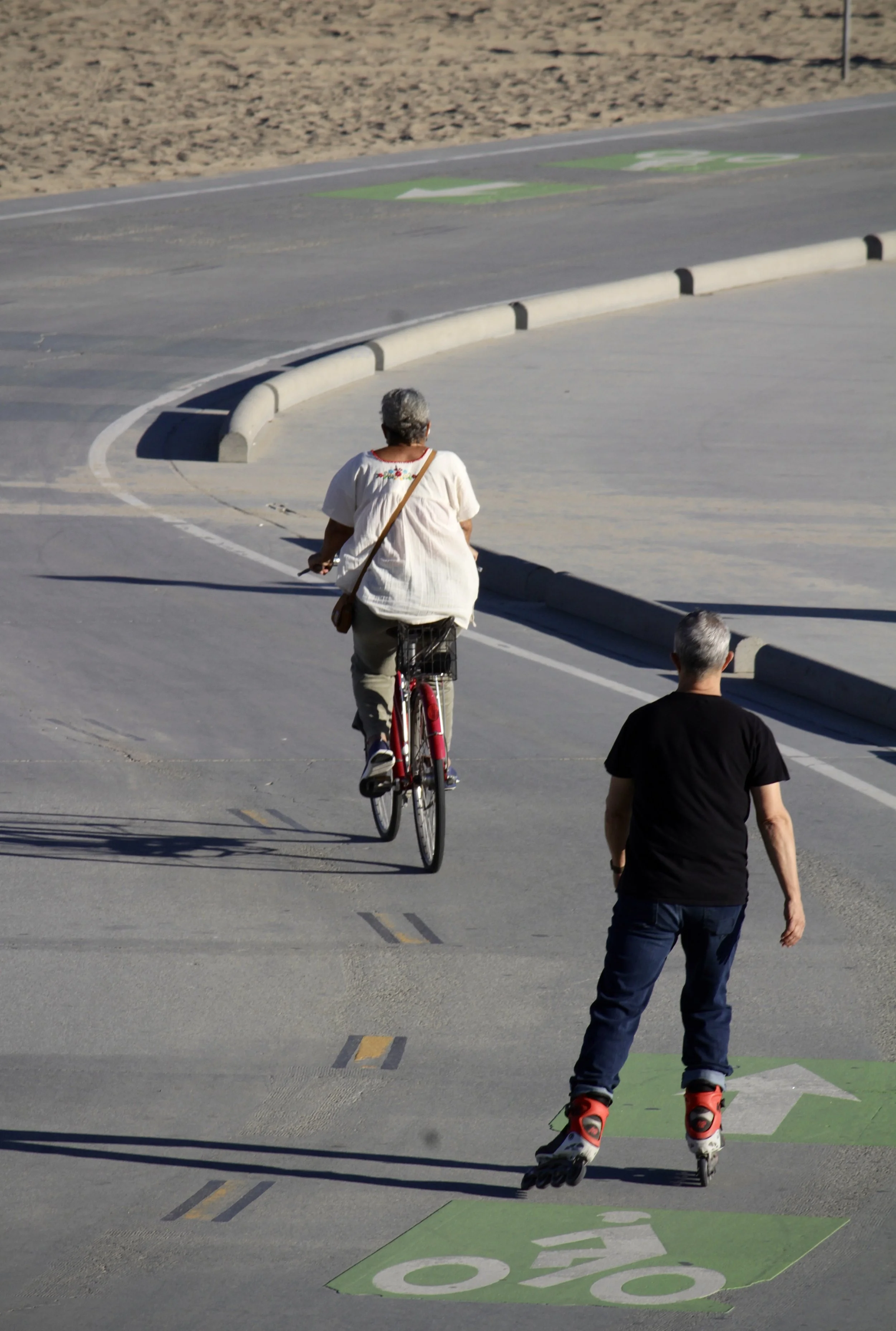 A person riding a bicycle and another person roller skating on a street with a green bicycle lane and a green 'STOP' painted on the ground.
