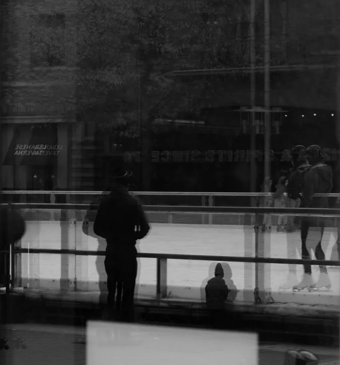 People ice skating on an indoor rink viewed through a glass window.