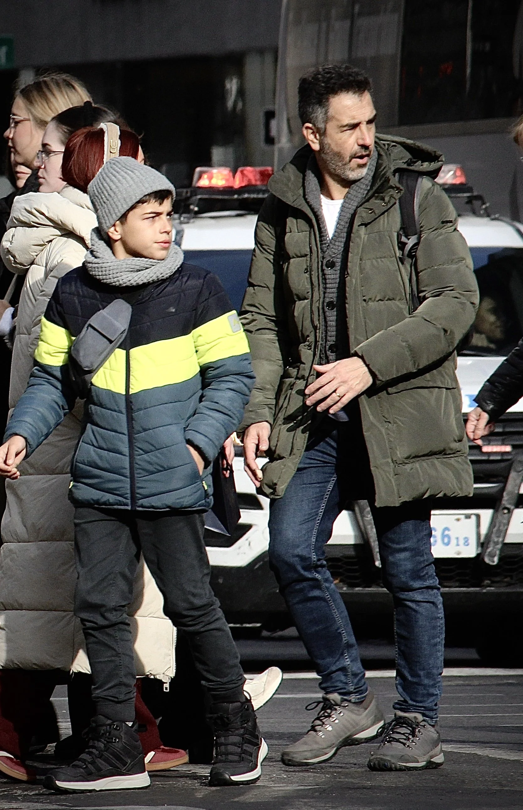 People standing on a city street near vehicles, wearing winter clothing.