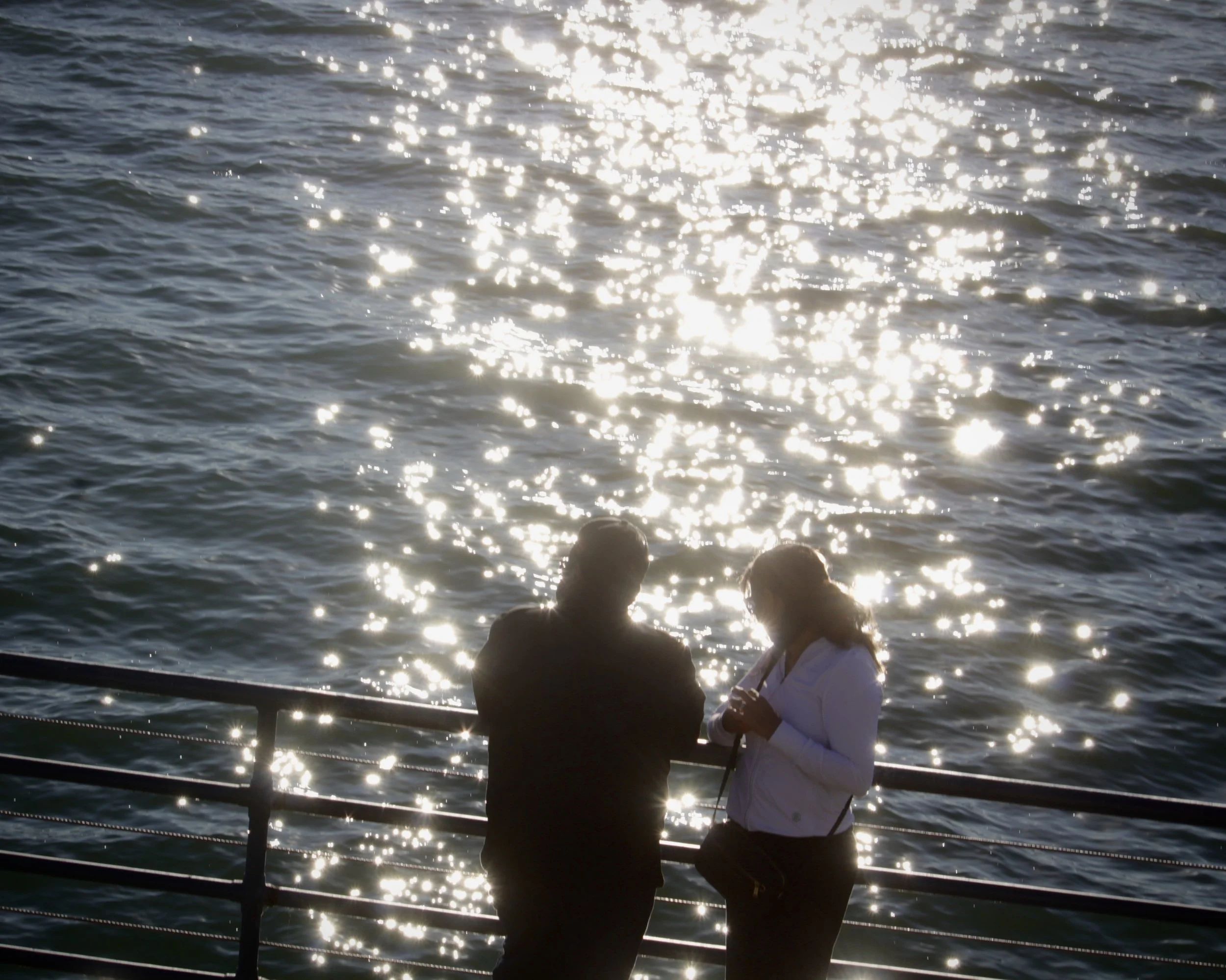 Two people fishing from a boat on the water during sunset, with sunlight reflecting off the surface.