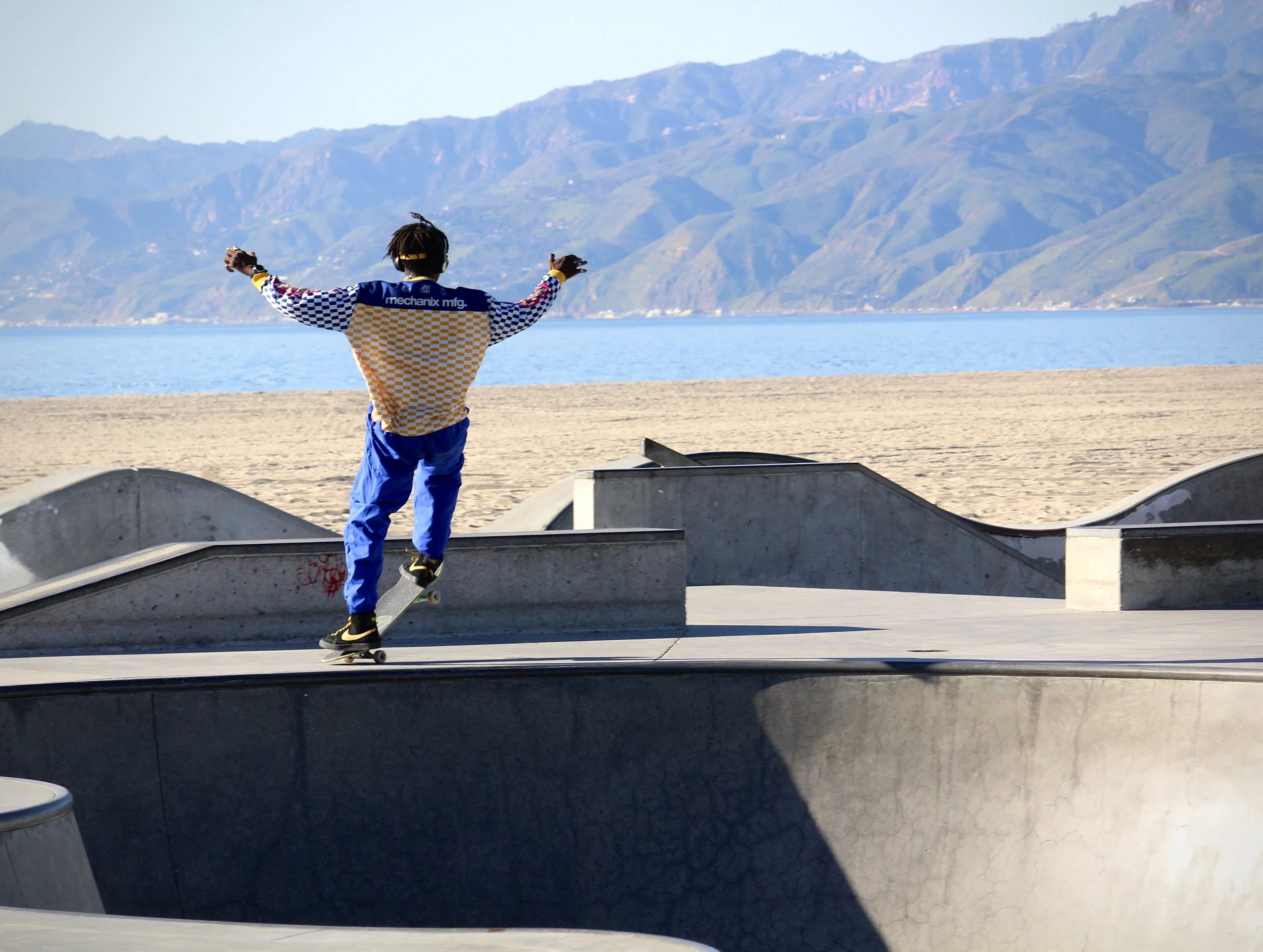 A person skateboarding at a skatepark by a beach with mountains in the background.