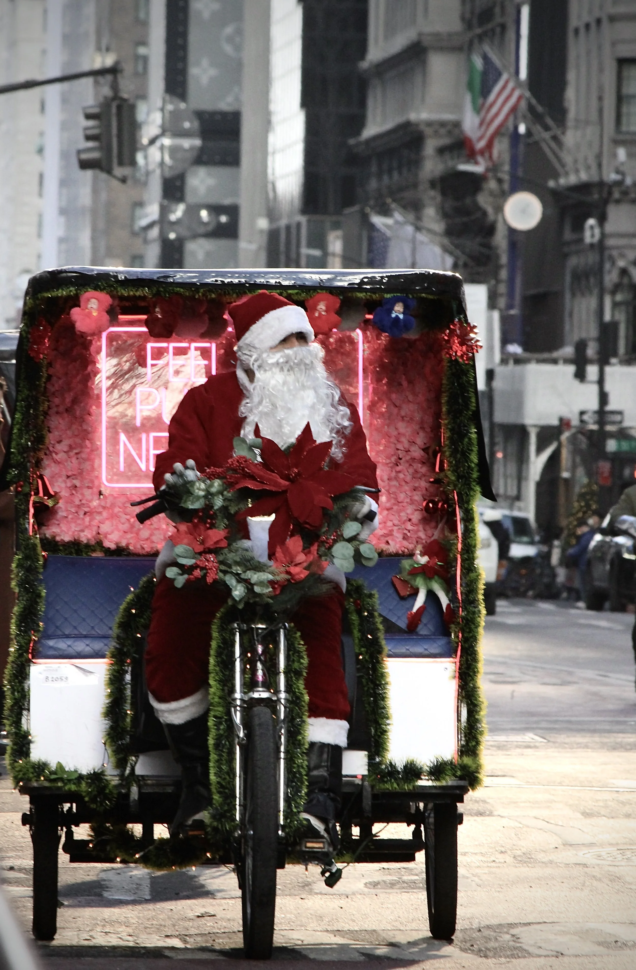 Santa Claus dressed in traditional red suit riding a decorated pedicab on a city street during Christmas time.