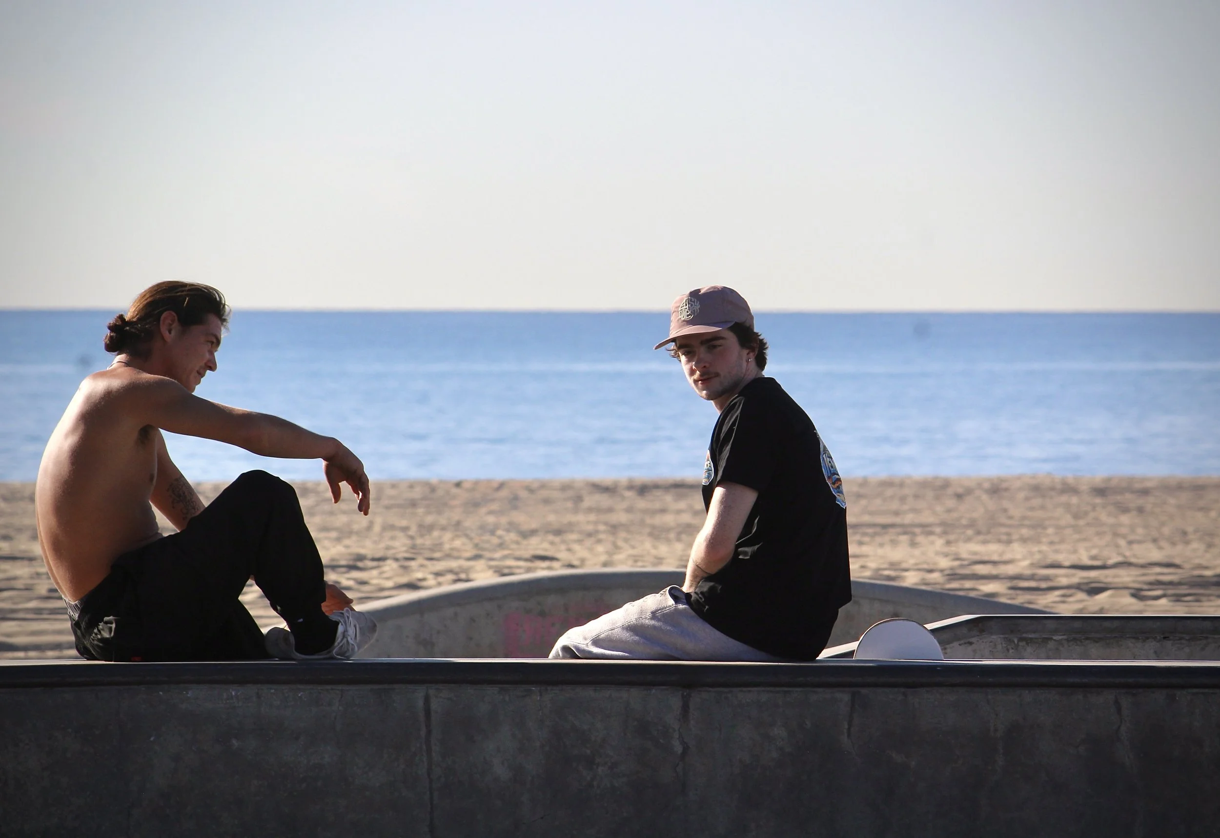 Two young men sitting on a boat at the beach with the ocean and sky in the background.