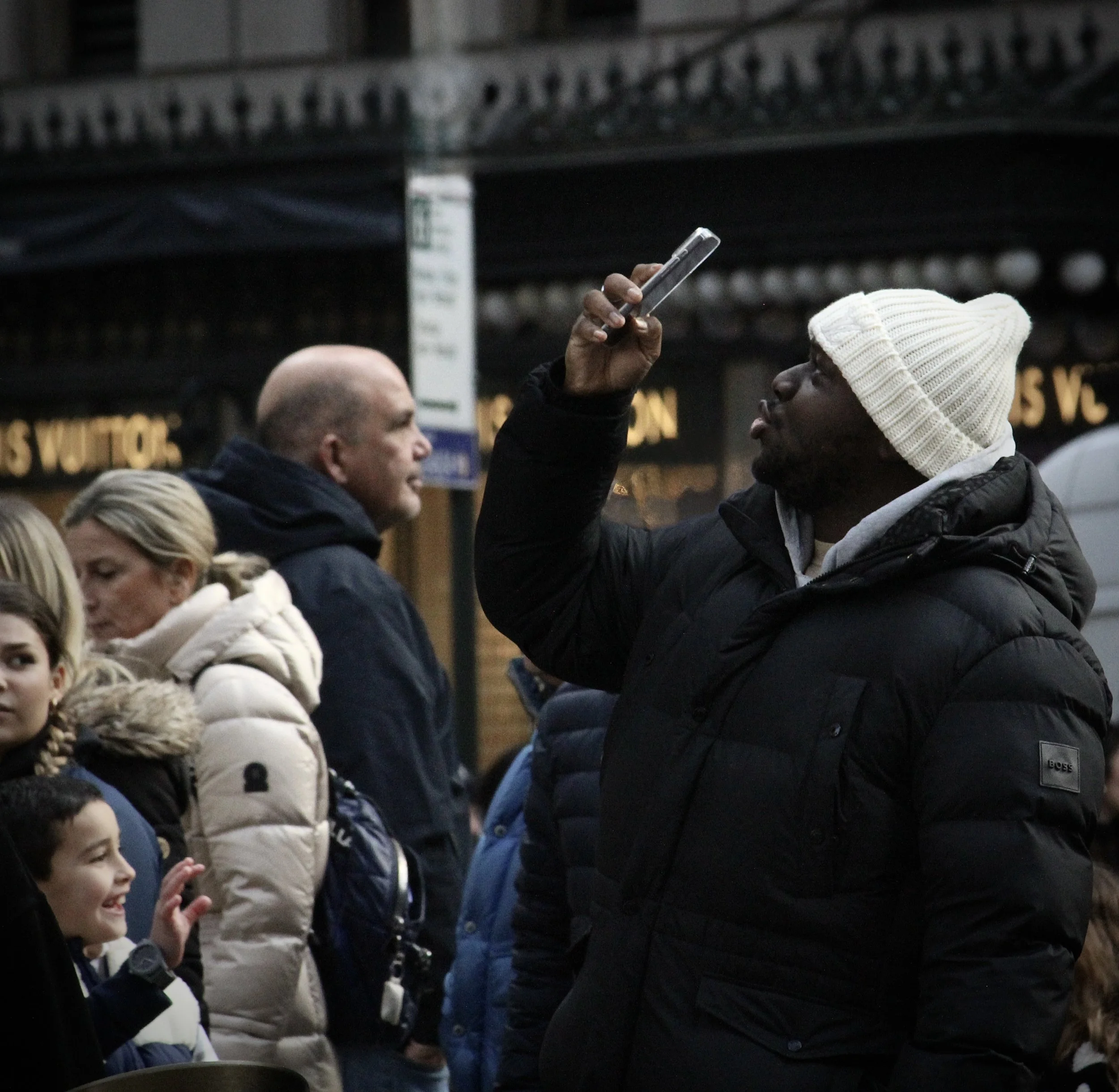 People standing in a line, with one person taking a photo or recording with a smartphone, in an urban setting at night.