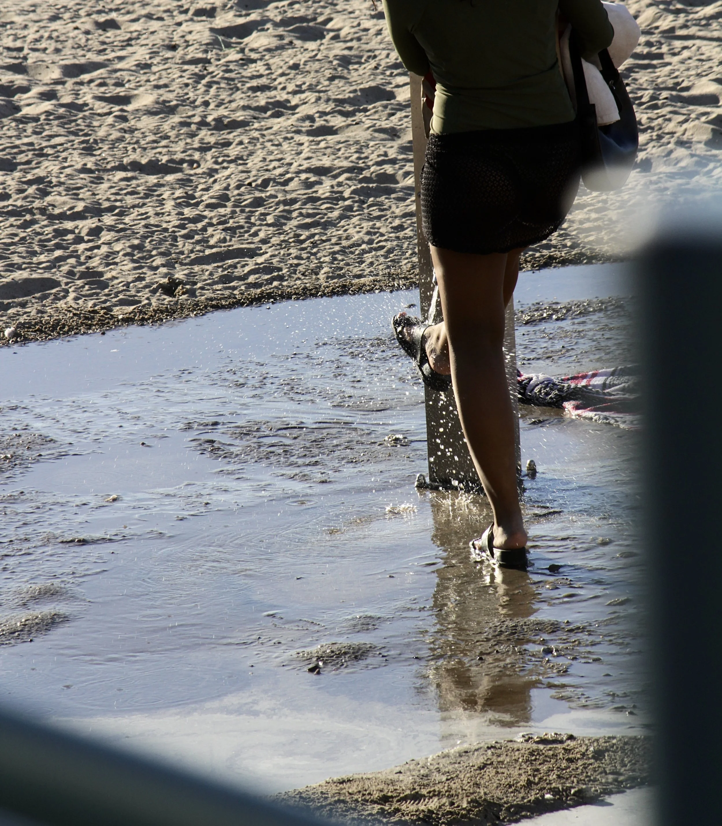 Person walking on the sandy beach near the water during sunset or sunrise, carrying a large bag.