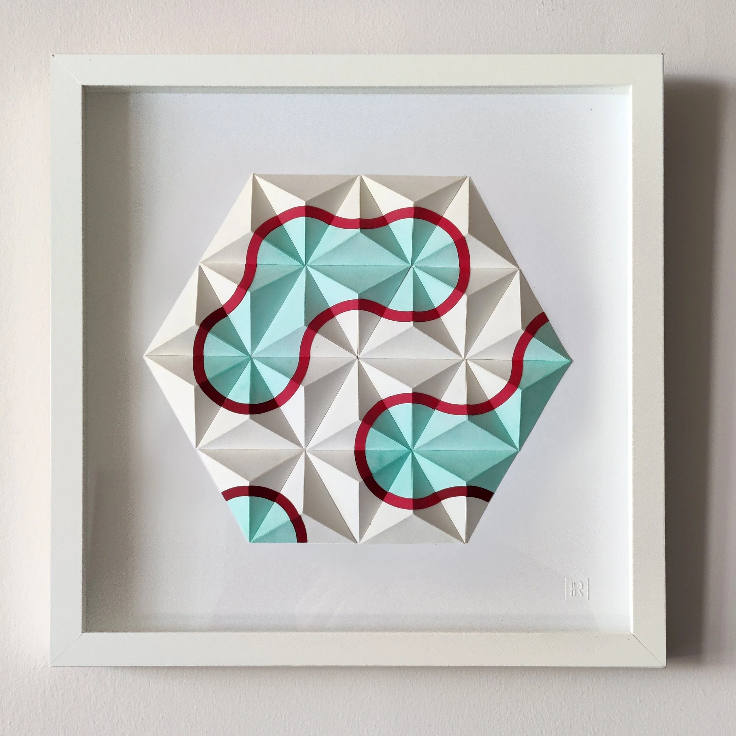 Framed geometric paper art with white, light blue, and red shapes forming a circular pattern.
