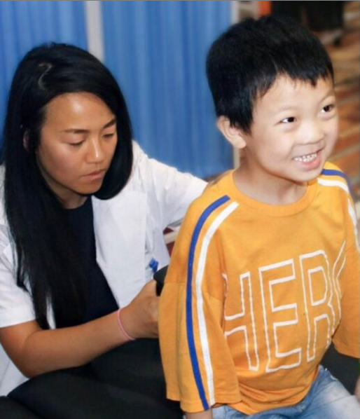 A healthcare professional appears to be checking a young boy's spine who is smiling, in a setting with a blue background.