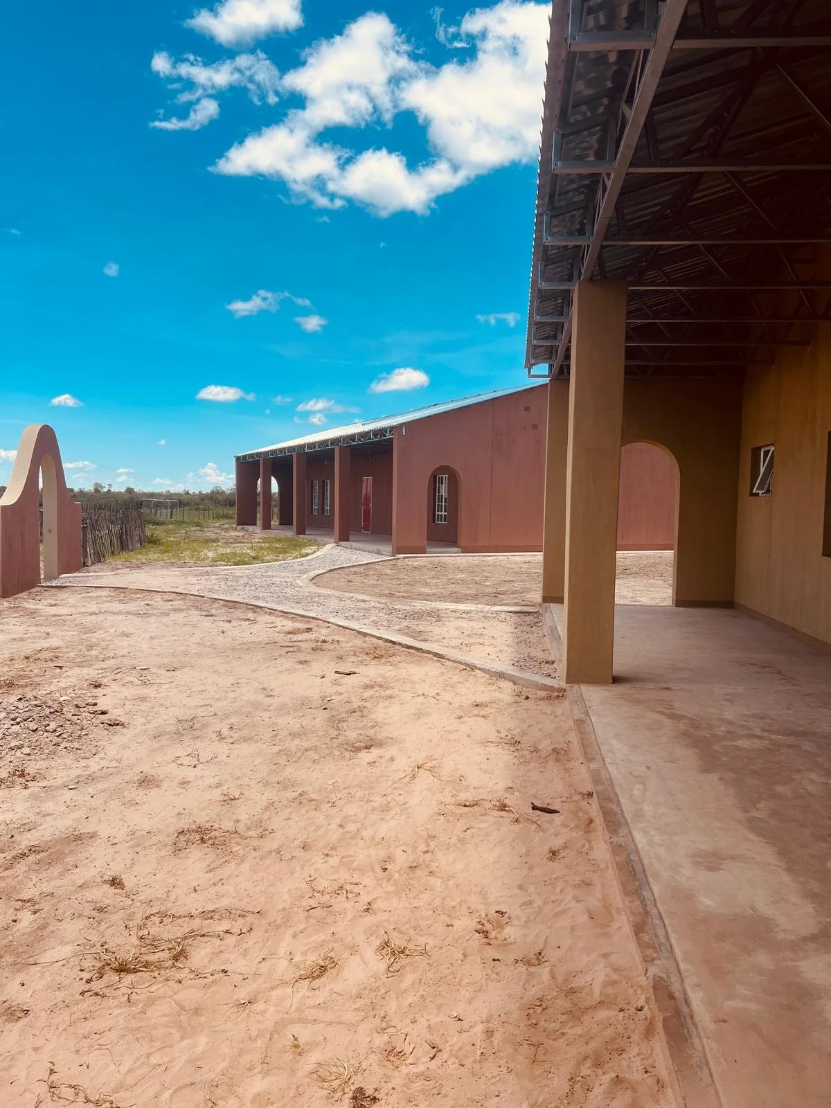 A partly constructed building on a dry, dirt landscape under a blue sky with scattered clouds.
