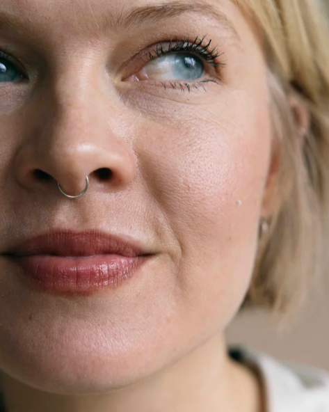 Close-up van een vrouw met blauwe ogen, een neusring en lichte make-up.