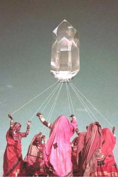 Vrouwen in traditionele kleding die een groot kristallen object vasthouden dat balanceert in de lucht.