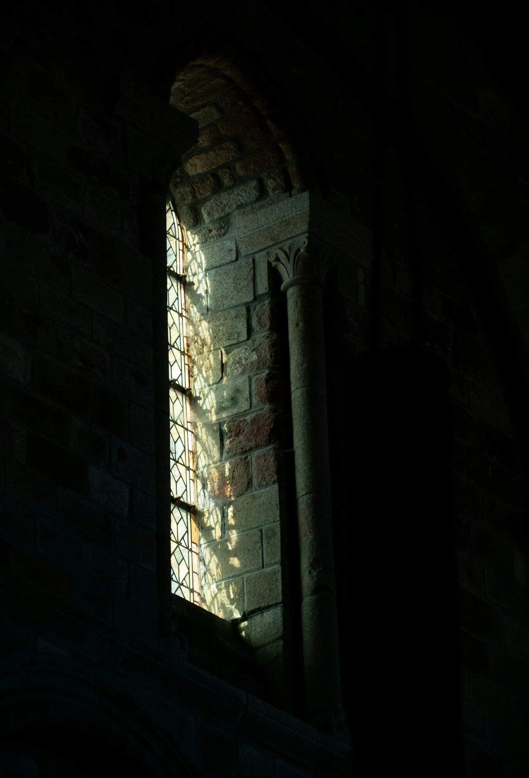 Sunlight streaming through a stained glass window, casting colorful shadows on a stone wall inside a church or cathedral.