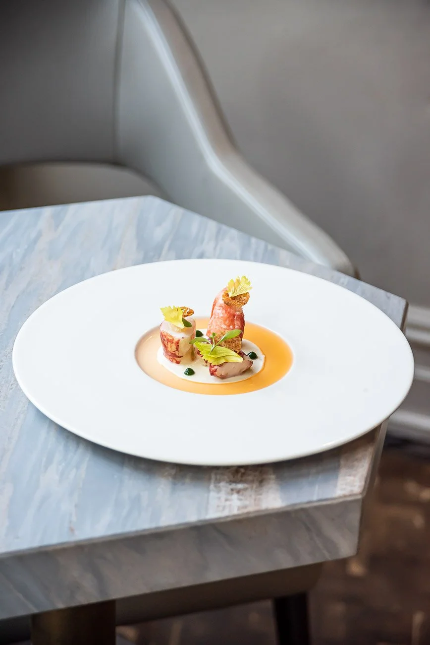 A gourmet dish with rolled and sliced meat, garnished with herbs, served on a white plate with a creamy sauce and orange-colored sauce accents.