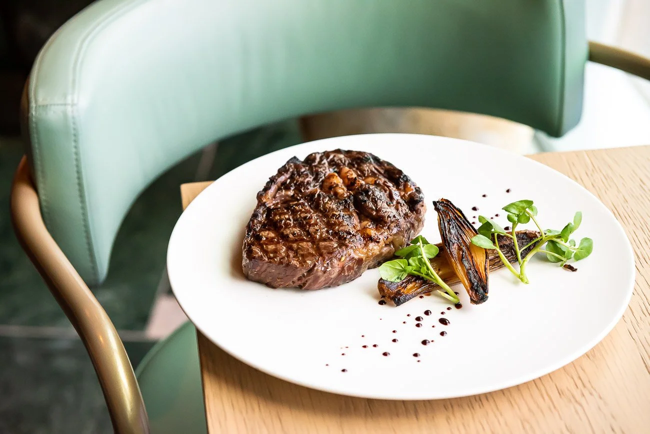 A plate of cooked beef with grilled vegetables and greens, garnished with sauce on a white plate.