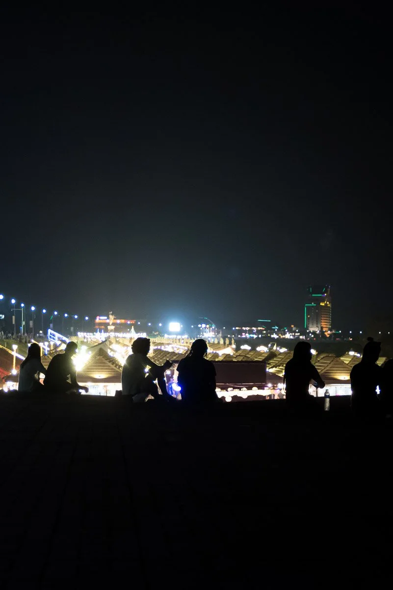 Group of people sitting and talking at night with city skyline and lights in the background.