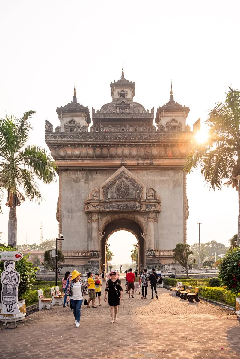 People walking near the Patuxai Victory Monument in Vientiane, Laos, during sunset.