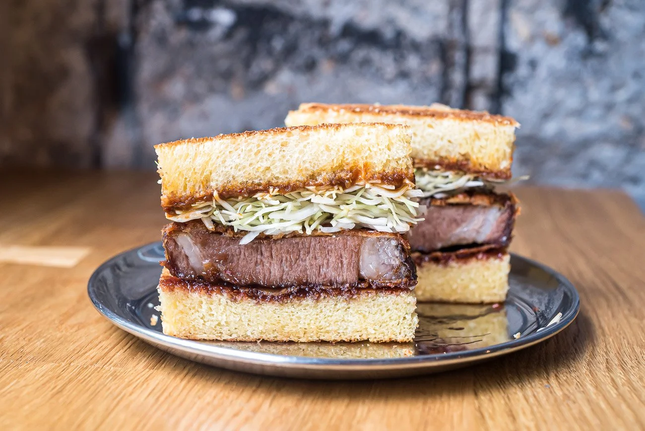 Close-up of a sliced roast beef sandwich with shredded cabbage and sauce on toasted bread on a metallic plate.
