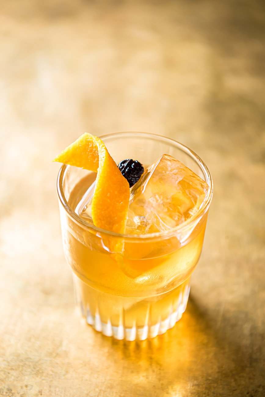 A glass of iced tea garnished with orange wedges and a blueberry, on a wooden surface.