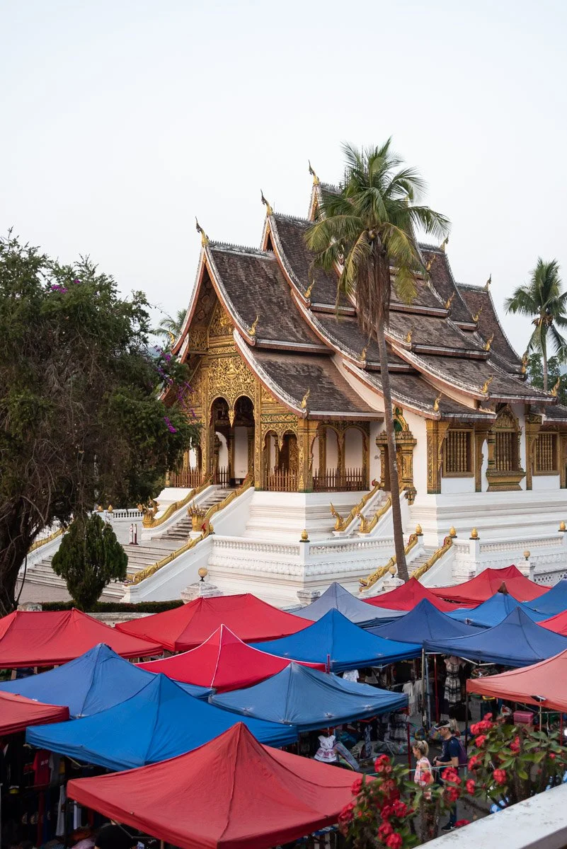 Traditional Thai temple with ornate gold decorations and multi-tiered roof, surrounded by tents and market stalls.