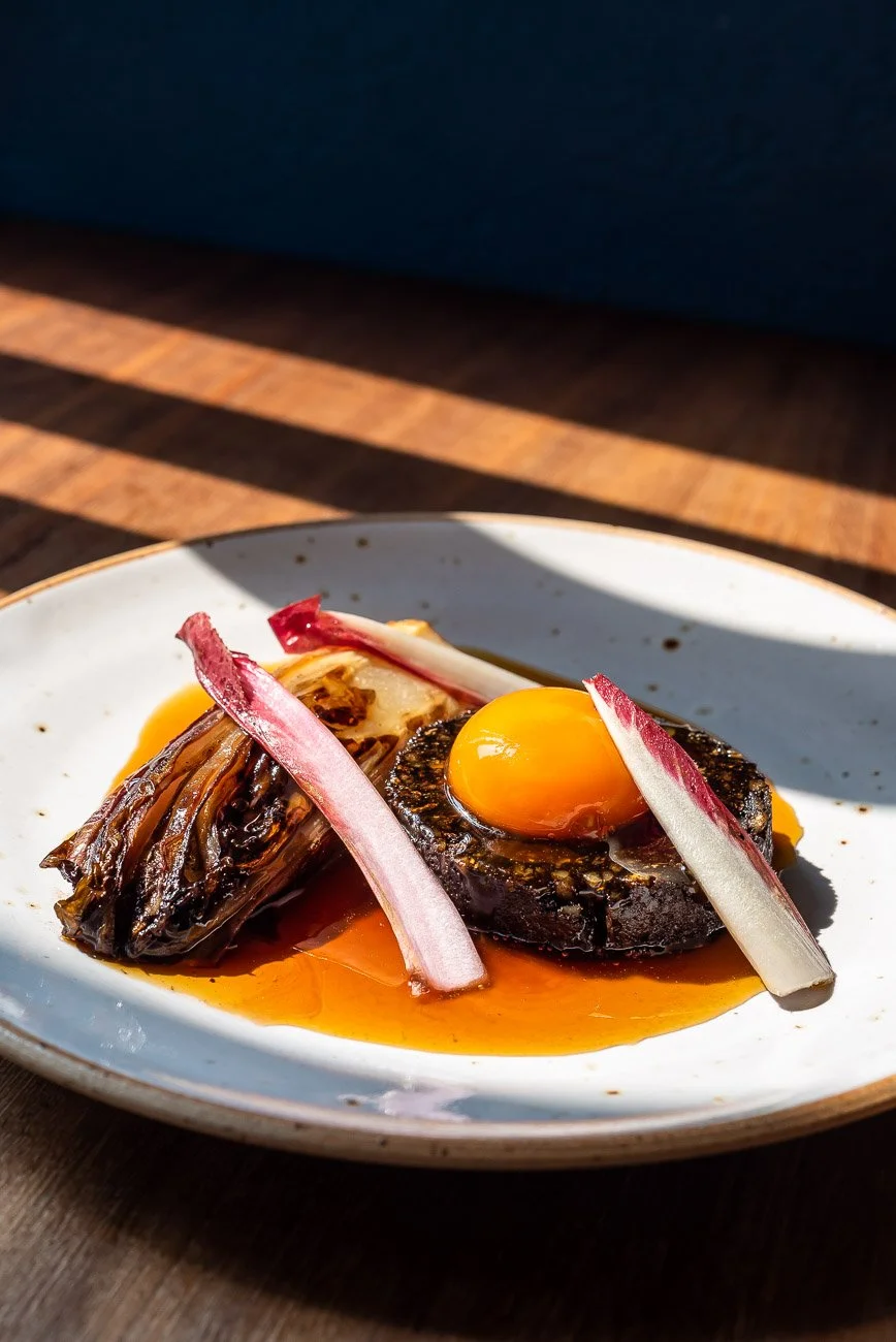 A plate of food with a fried egg on top of a fried piece of meat, garnished with pickled vegetables, served with sauce on a white ceramic plate.
