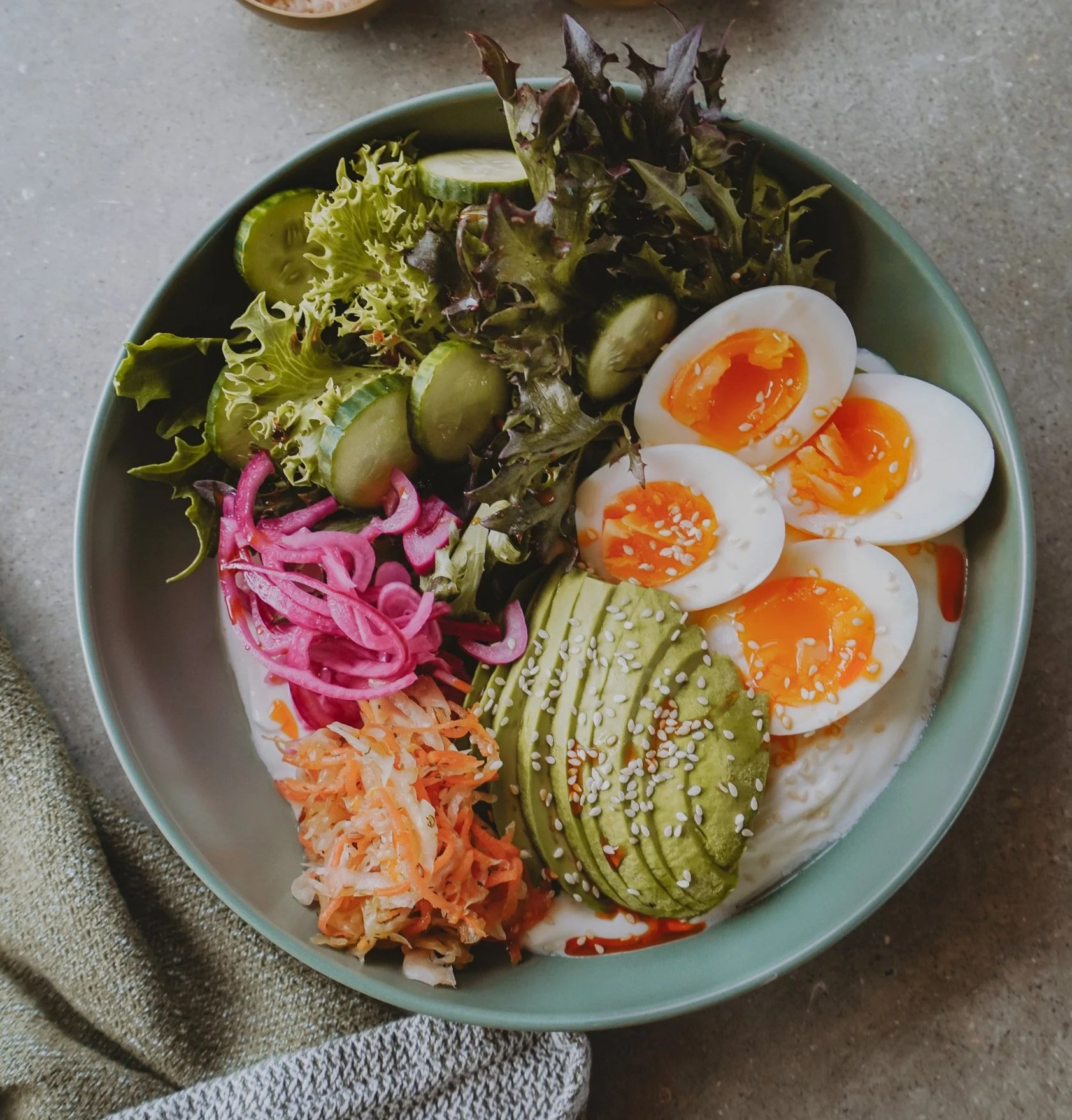 Bowl of salad with soft-boiled eggs, sliced avocado, mixed greens, cucumber, pickled onions, shredded carrots, and dressing.