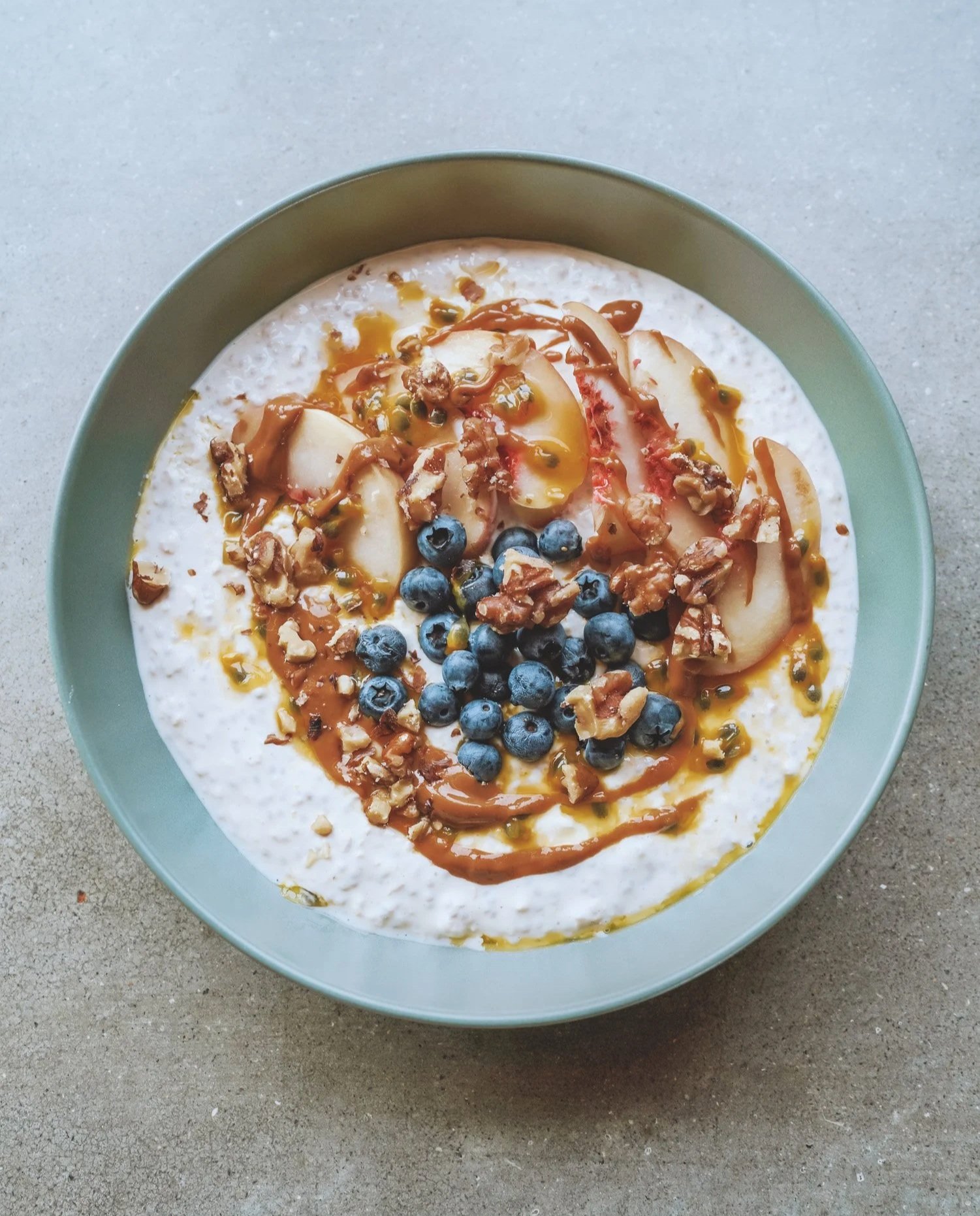 Bowl of overnight oats topped with blueberries, sliced apple, chopped nuts, honey, and a drizzle of caramel sauce.