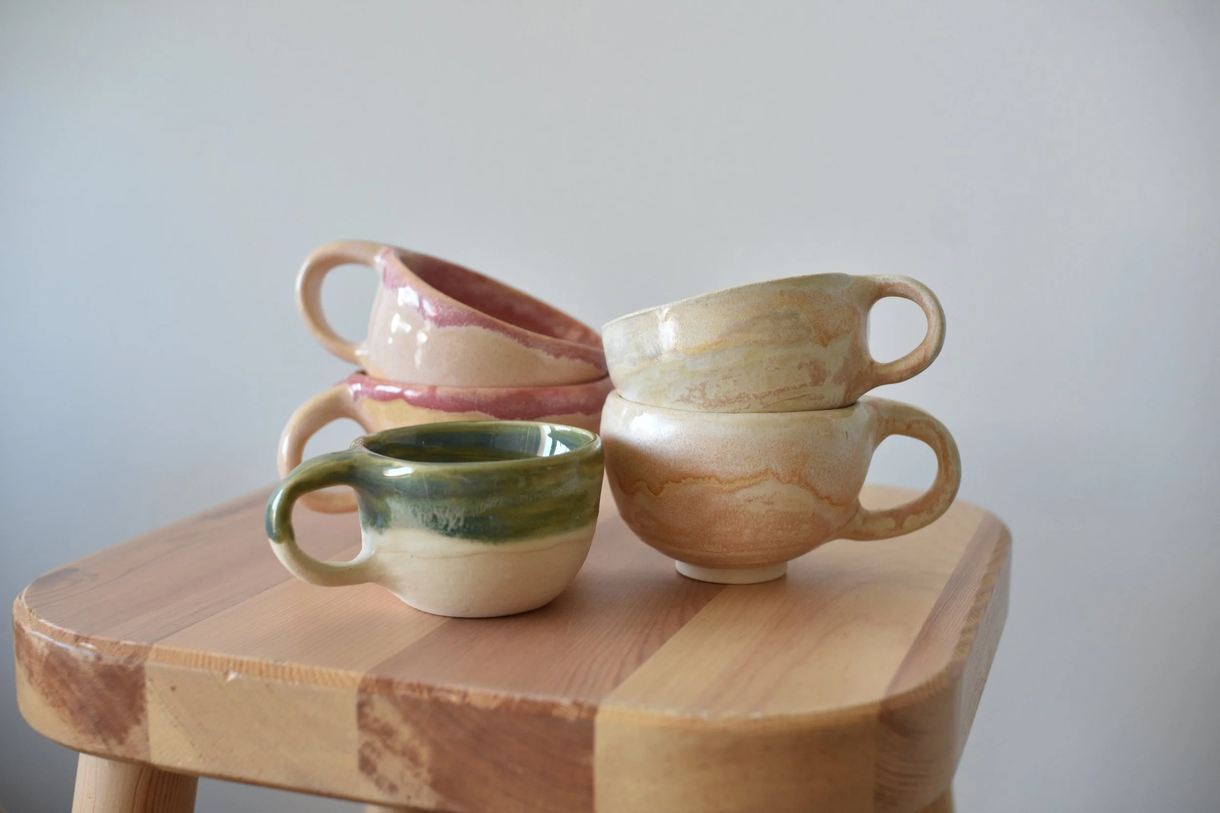 Stacked ceramic espresso mugs / cups with different pastel colors on a wooden table.