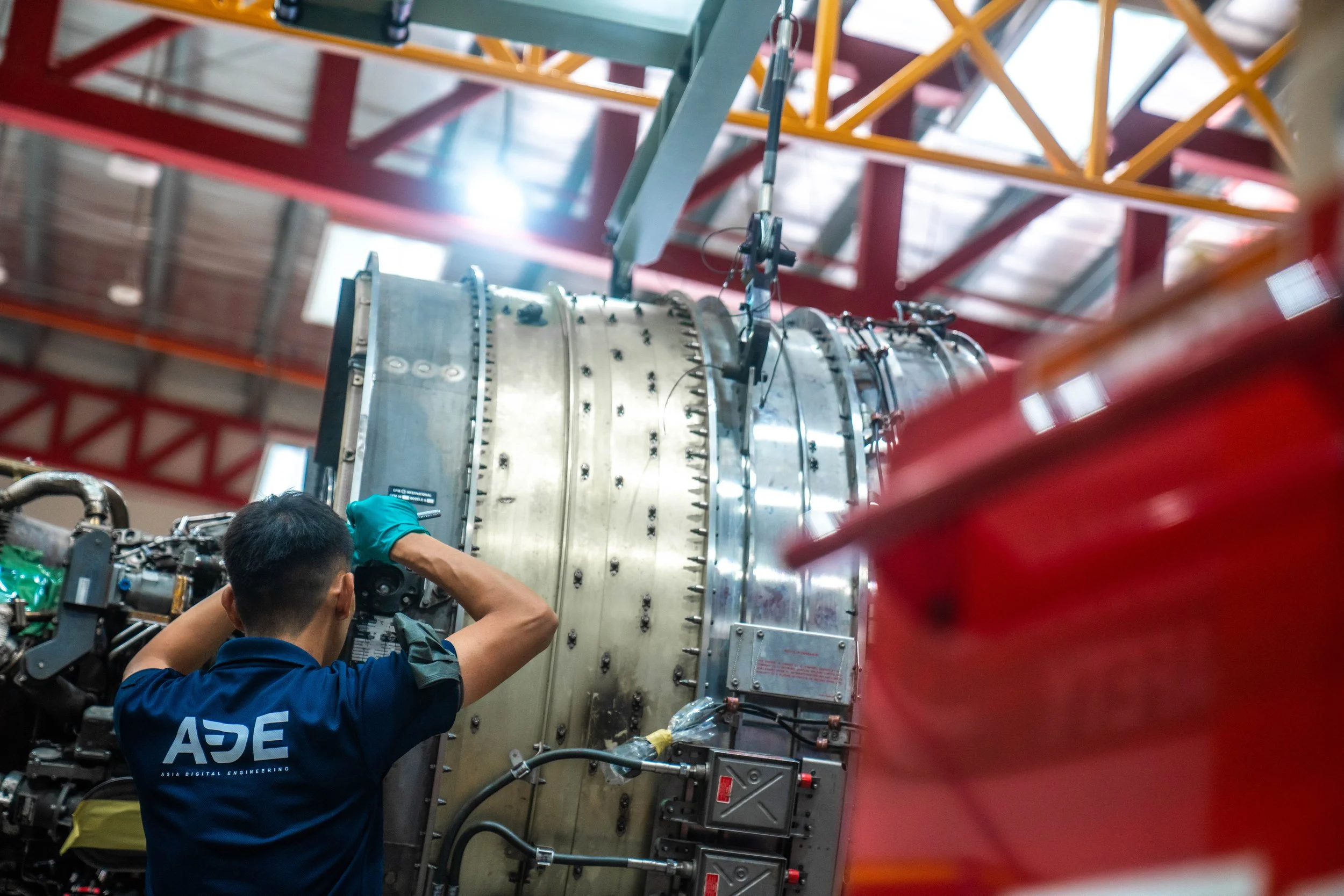 Two engineers working on a large scientific instrument or machine inside a laboratory or manufacturing facility with red and yellow structural beams in the background.