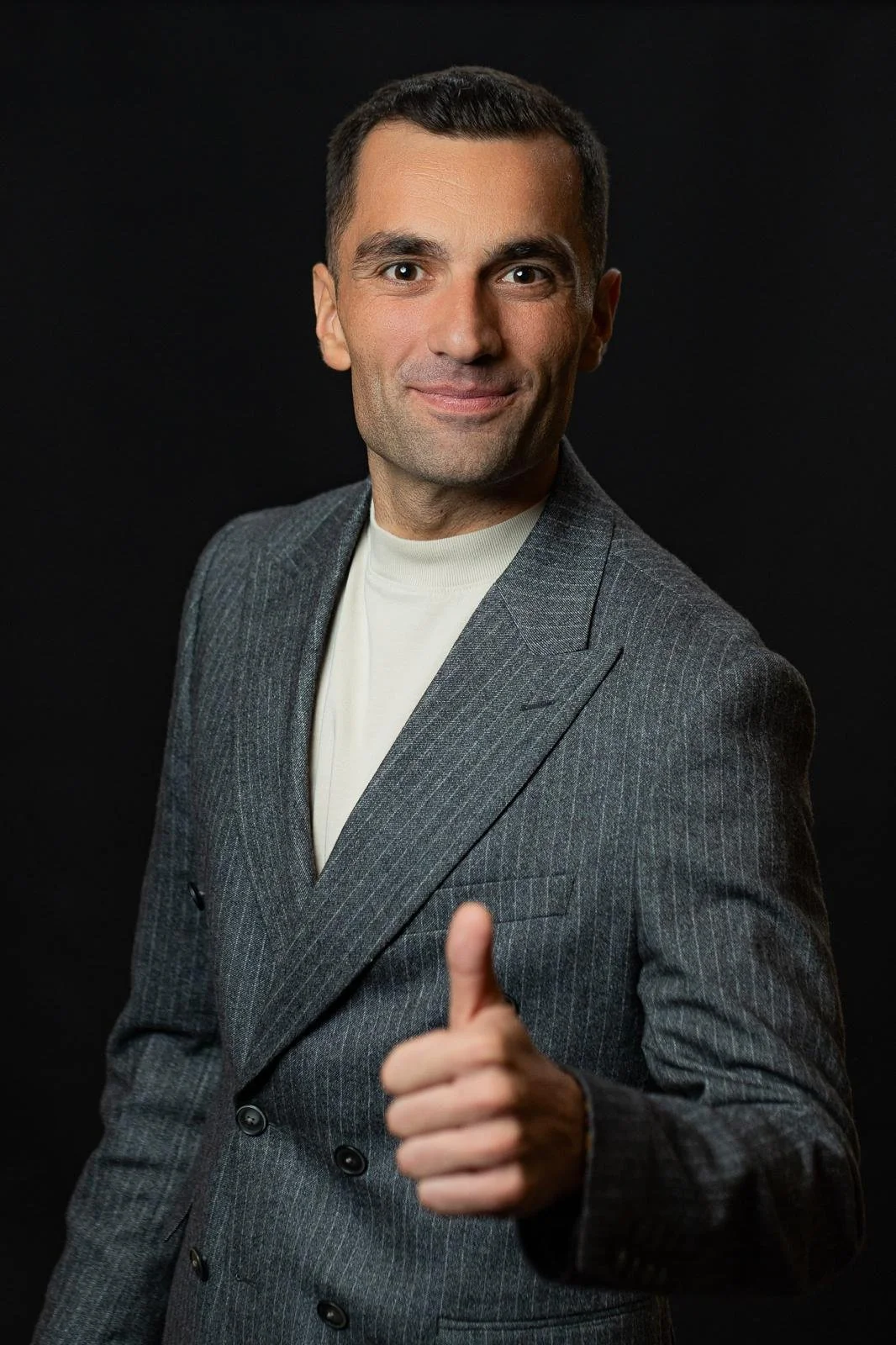 Ursu Iulian în costum, zâmbind și făcând semnul thumbs up, invitând la o discuție 1 la 1 despre programul Trade Grader.