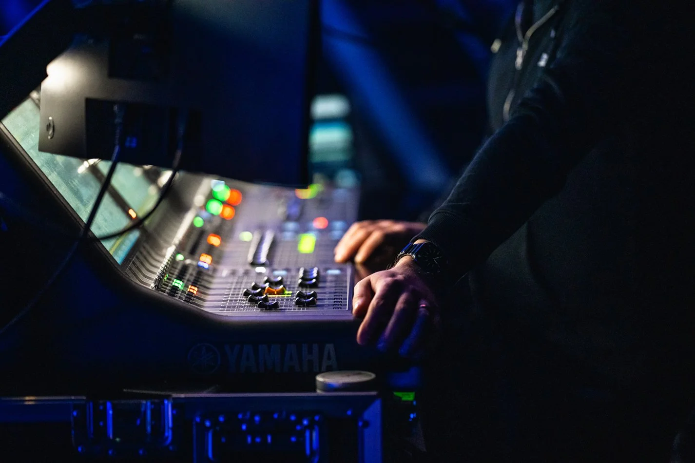 Person som justerar ljudutrustning på en Yamaha mixer i en mörk miljö, med olika knappar och skärmar som lyser.