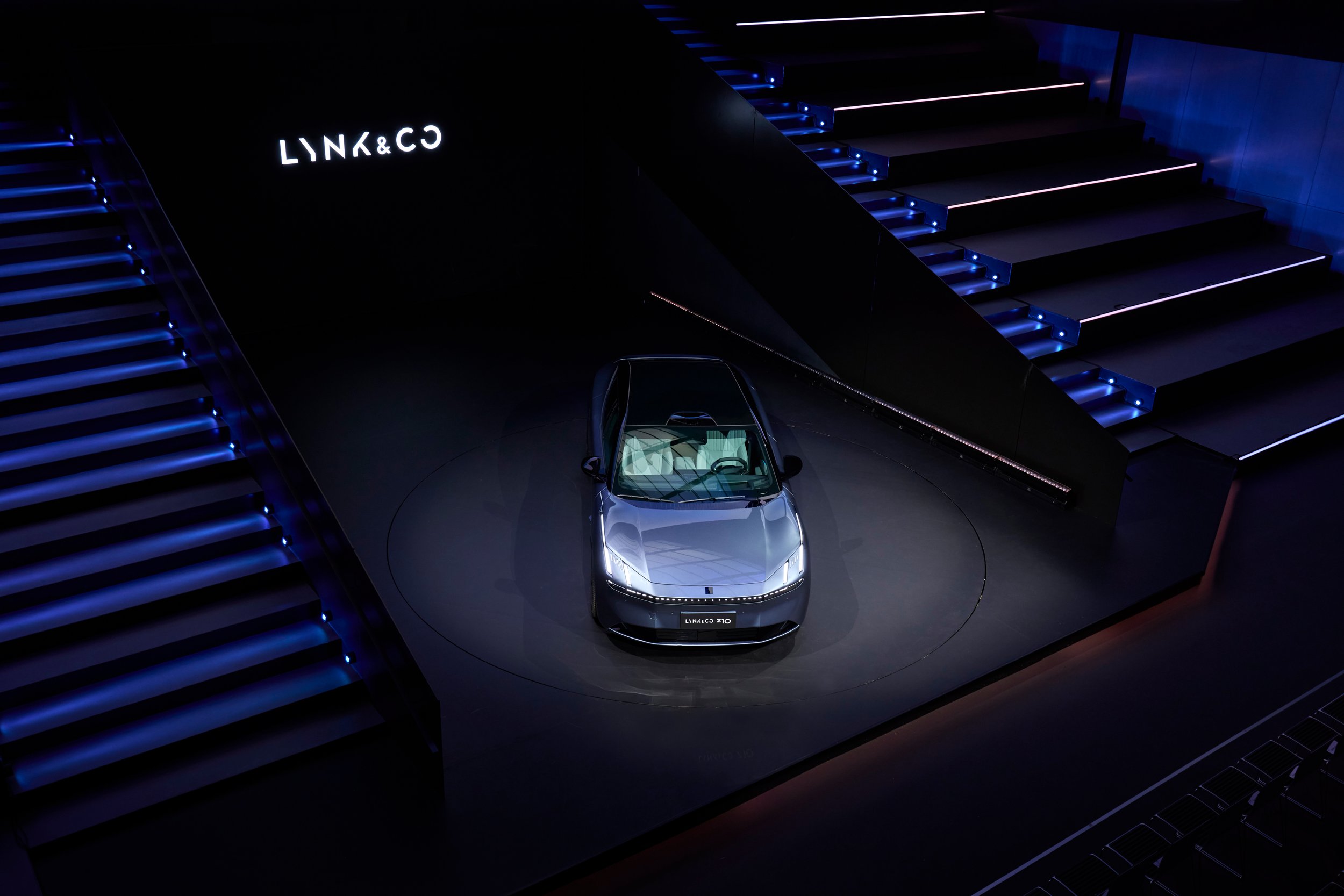 En futuristisk bil utställd under en mörk miljö med blå belysning och en ljus upplyst skylt som säger "LYNK&CO".