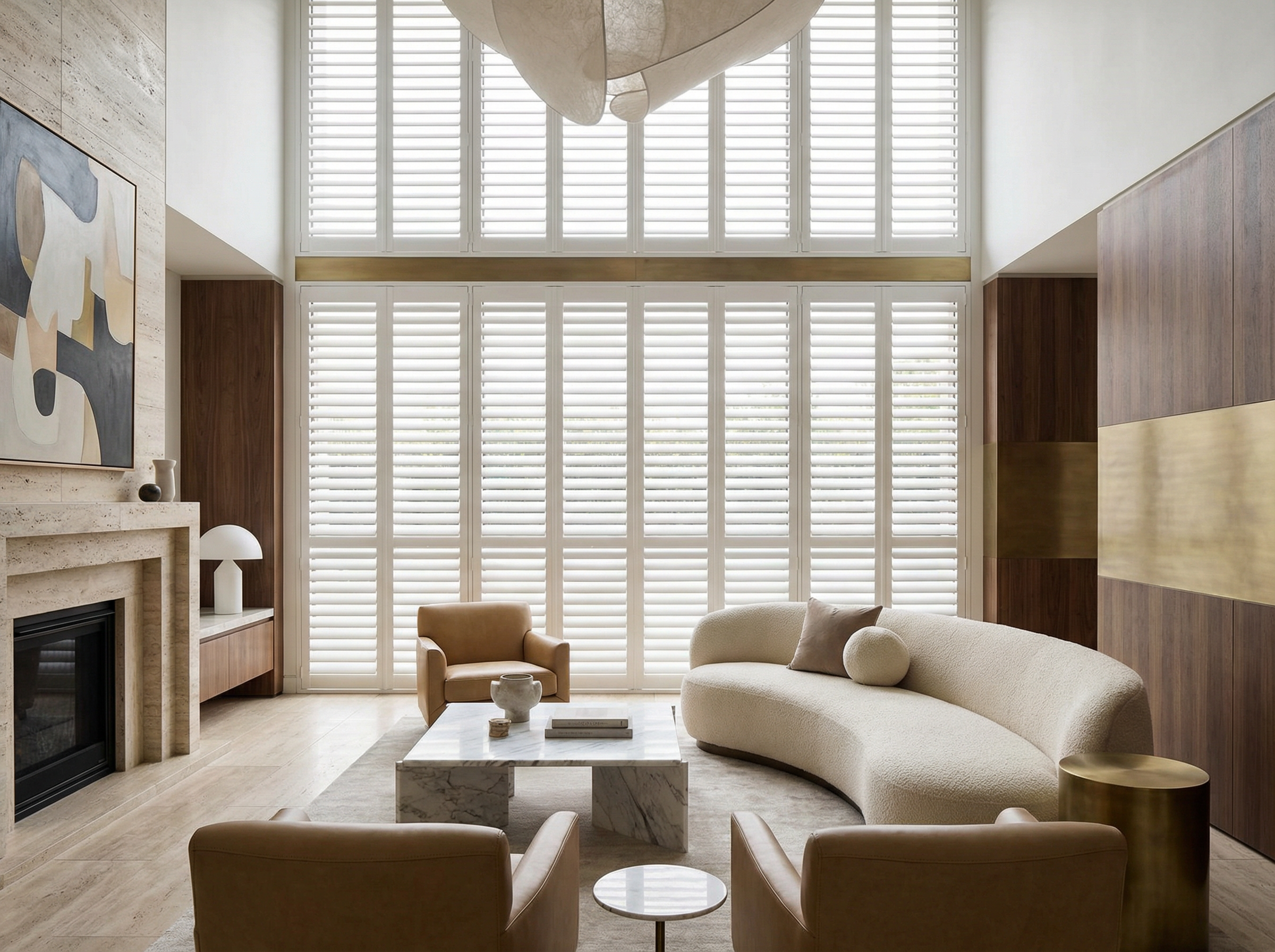 Modern living room with large window covered by white plantation shutters, beige curved sofa, tan armchairs, marble coffee table, abstract wall art, and minimalistic decor in neutral tones.