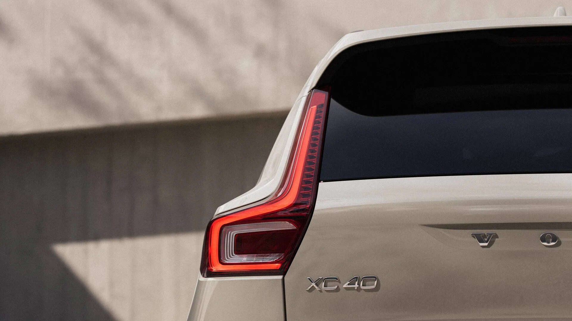 Close-up of the rear of a beige Volvo XC40 SUV, showing the tail light, model badge, and Volvo emblem.