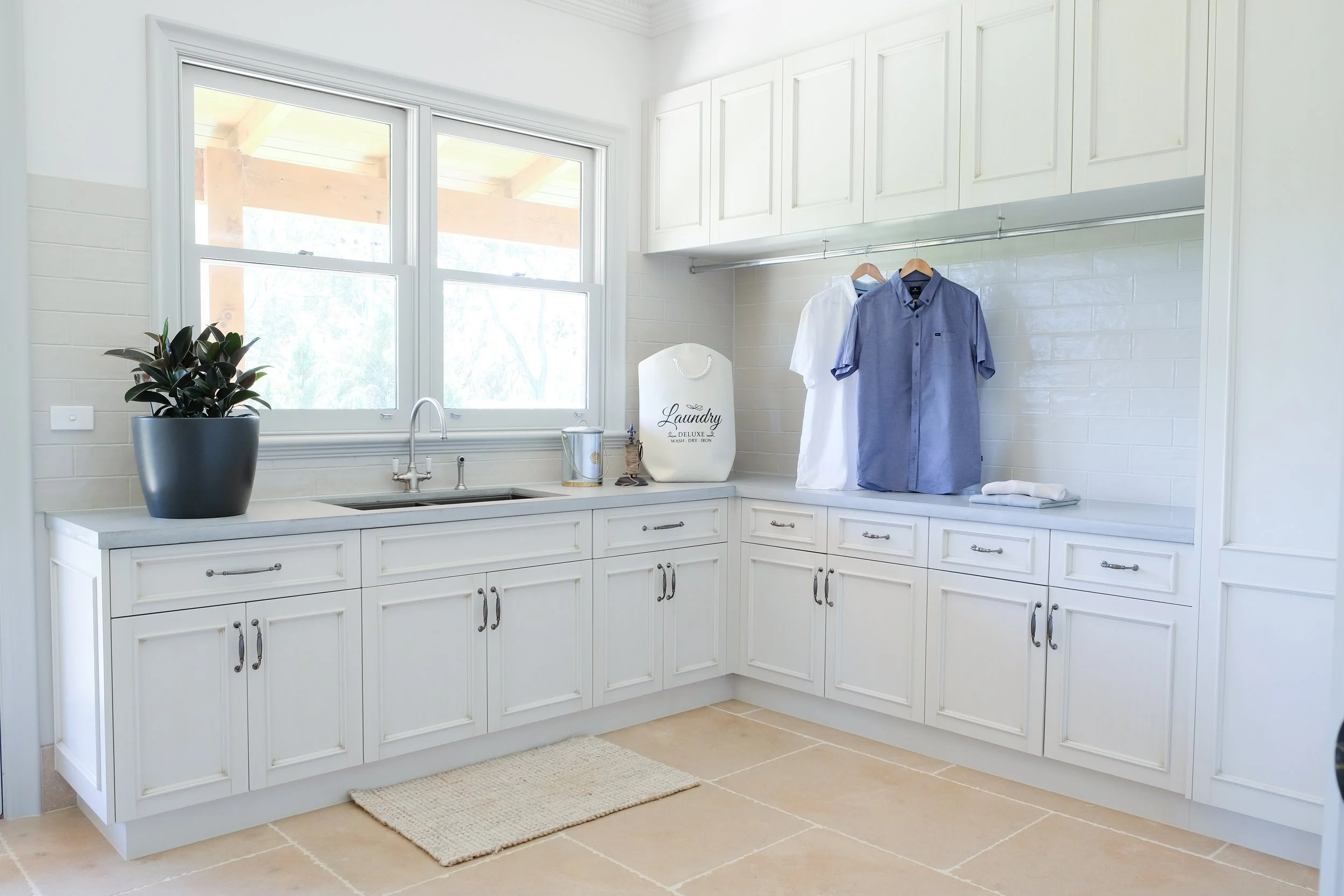 Laundry, cream coloured traditional style cabinetry, hanging rod for clothes, limestone floors, bronze undermount sink, English tapware