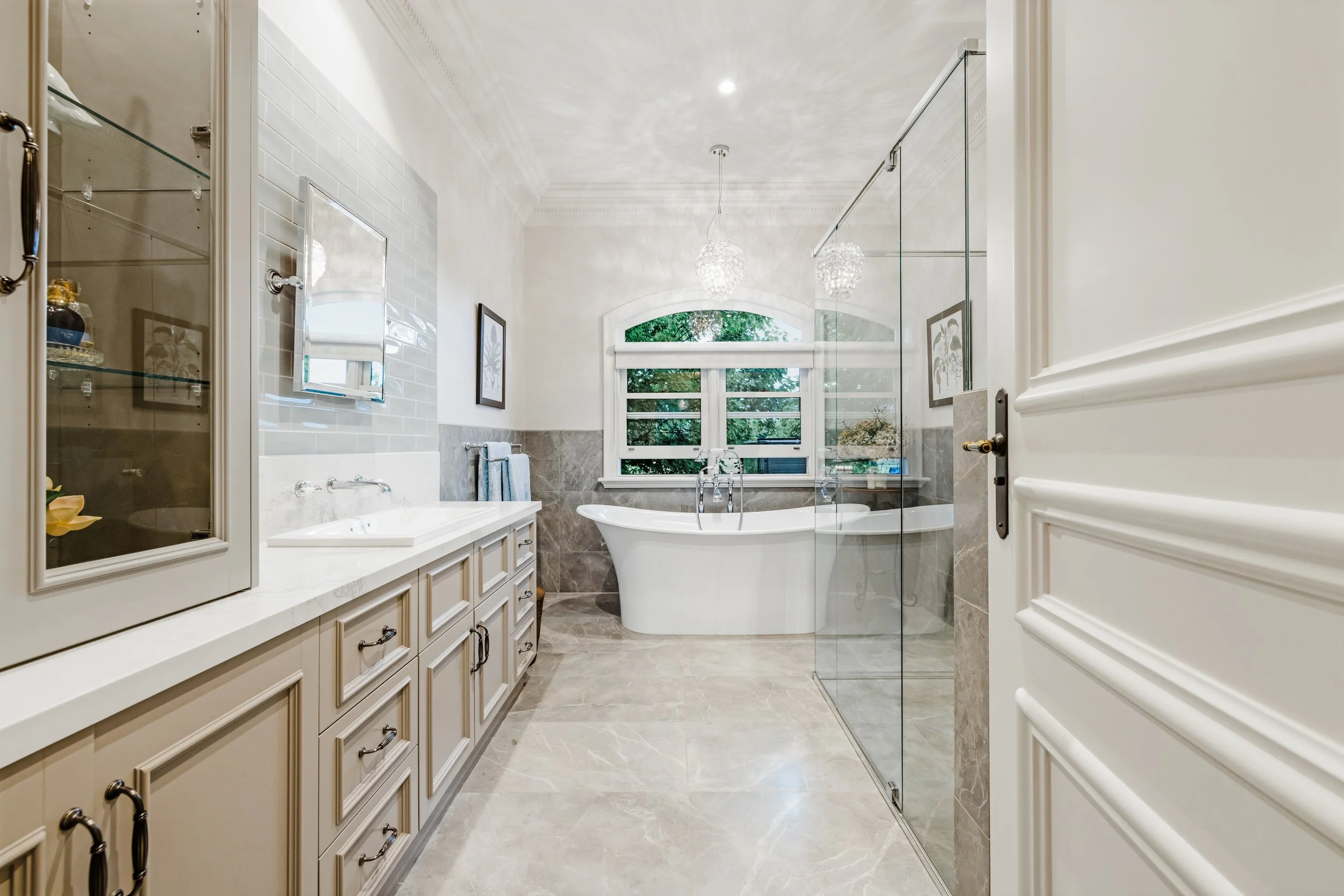 Luxury bathroom, Porcelain tiles with light blue feature wall behind cabinetry. Grey coloured cabinetry with wall hung taps over drop in basin. Pivot mirror. Freestanding bath, frameless glass shower