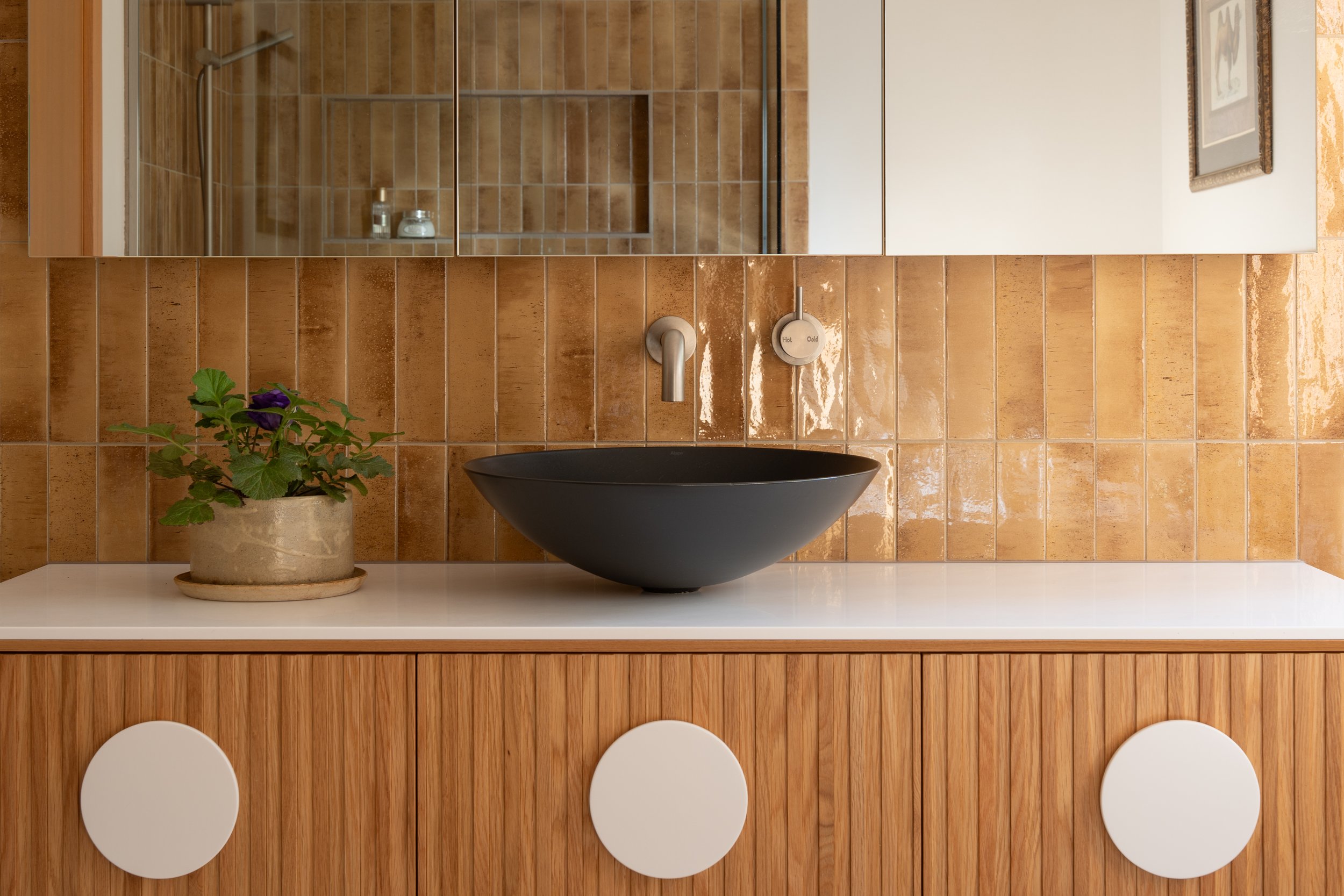 Luxury Bathroom, steel black above counter basin, Corion 12mm benchtop and round vanity handles with oak coloured vanity unit with lineal detailing, mustard coloured porcelain tile feature wall