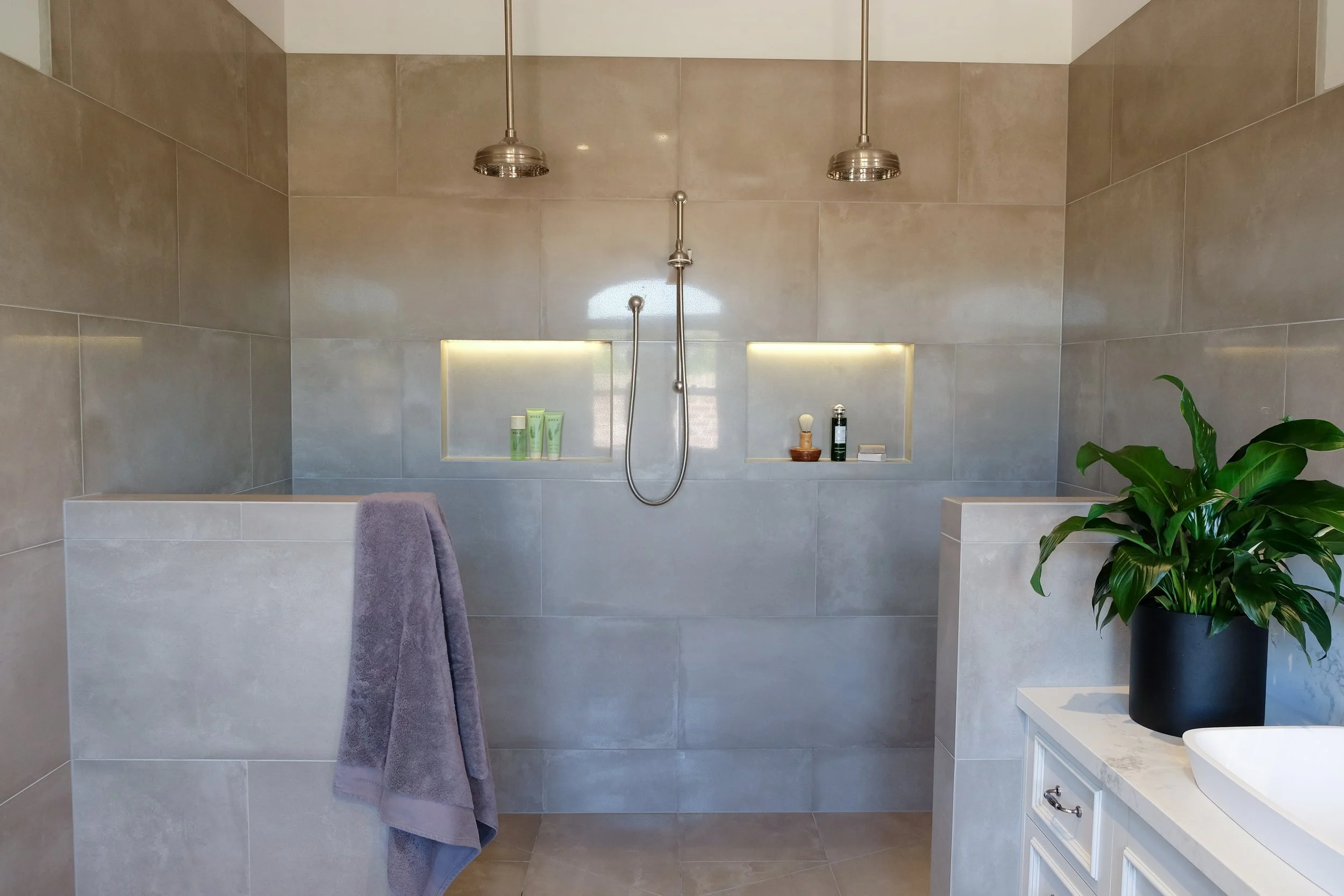 walk in shower for two. two nib walls either side of entry into shower. Porcelain soft grey  tiles, twin ceiling drop shower roses, central rail shower, twin niches with LED lighting