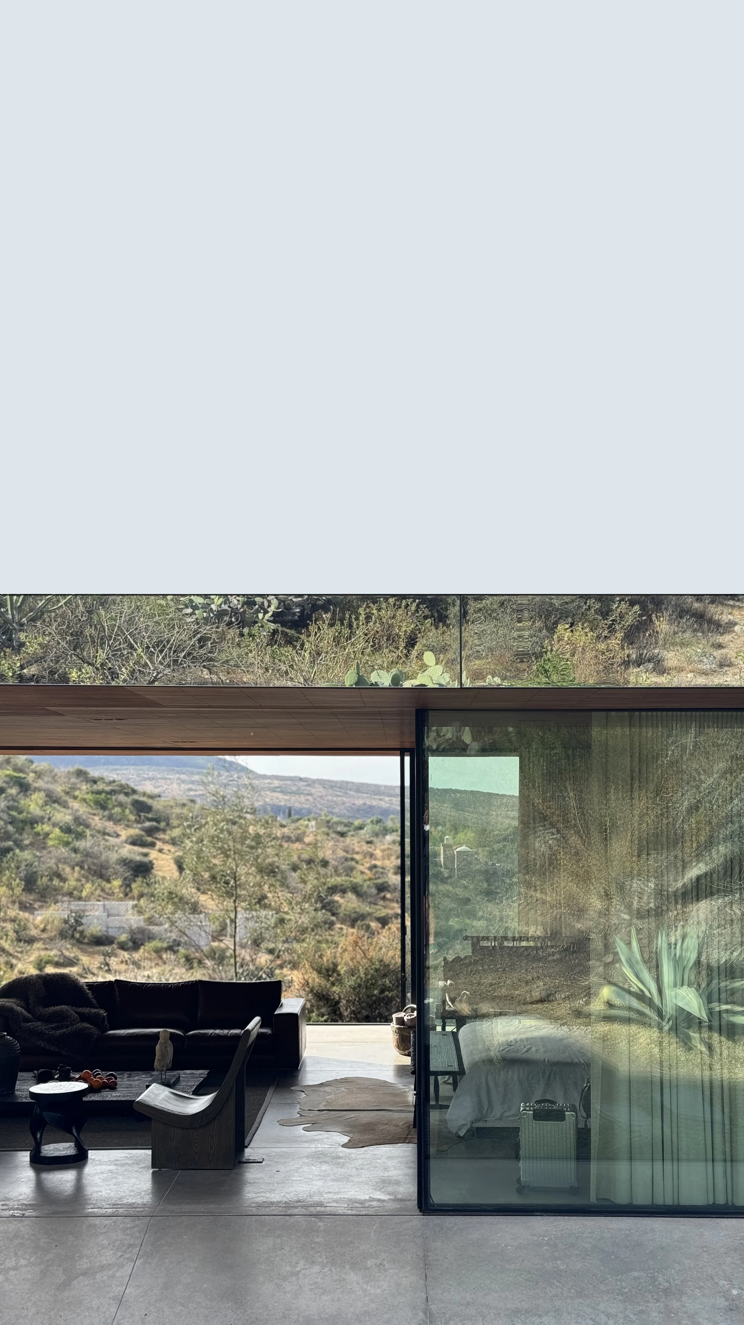 Living room with black sofa, wooden chair, cowhide rug, and large glass sliding doors opening to a view of hills and trees.
