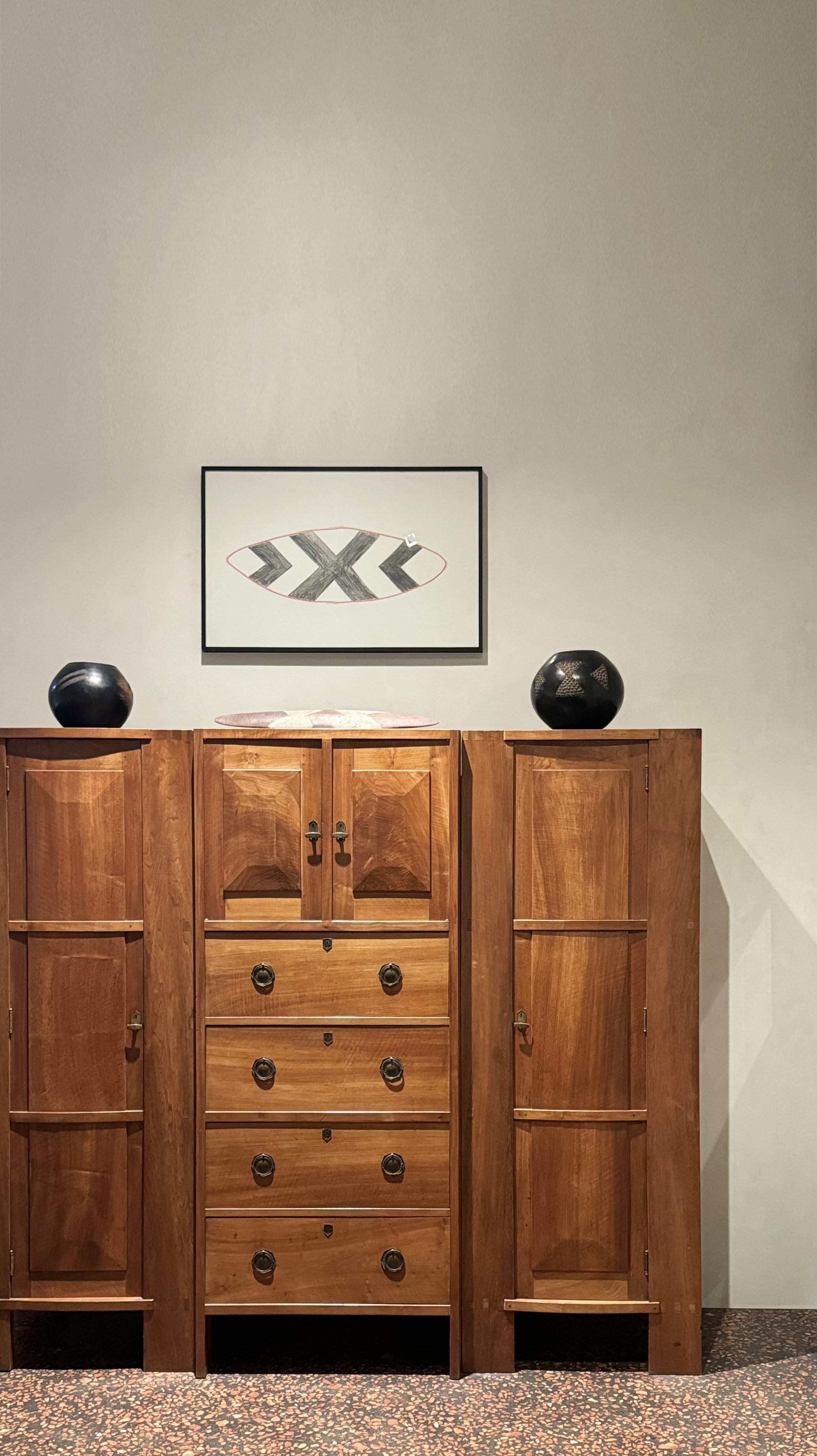 A wooden cabinet with four drawers and four doors, two black vases on top, and a framed artwork with angular black shapes on the wall behind.