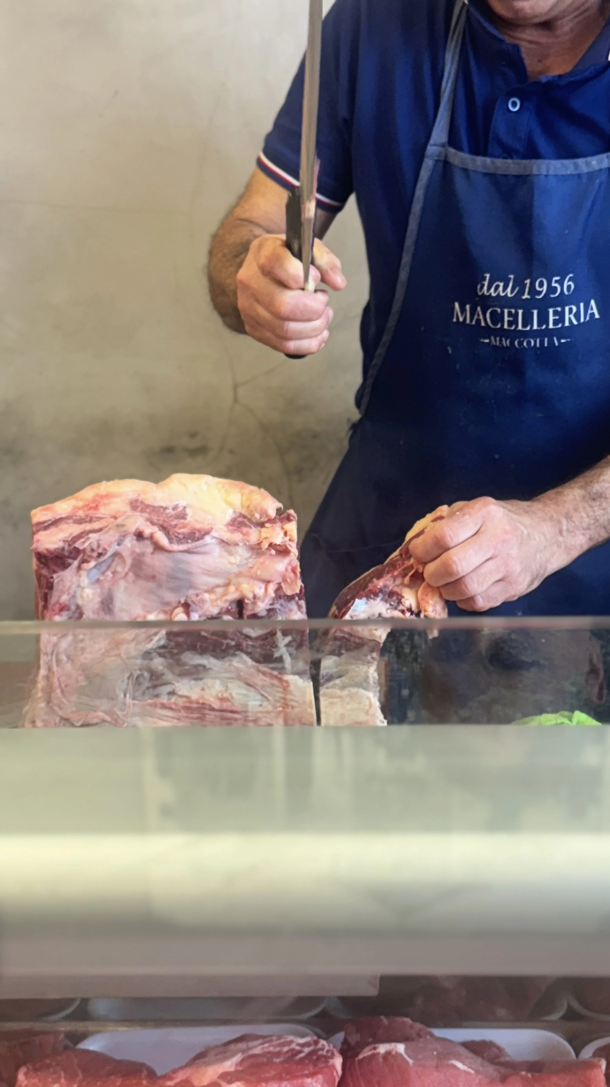 Butcher slicing meat behind a glass display case in a butcher shop.