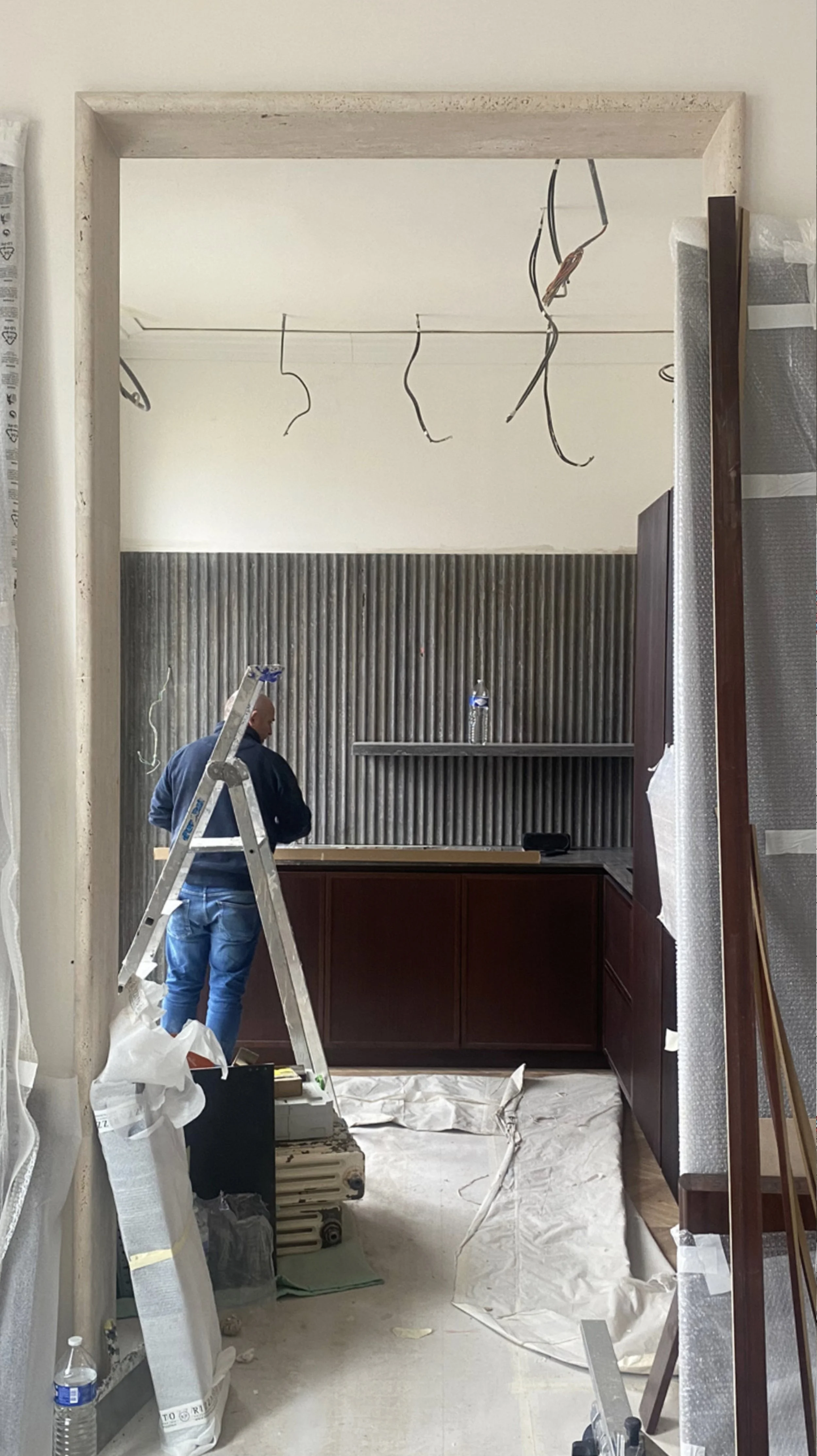 Interior of a room under renovation with a man working, ladder, construction materials, and exposed wiring.