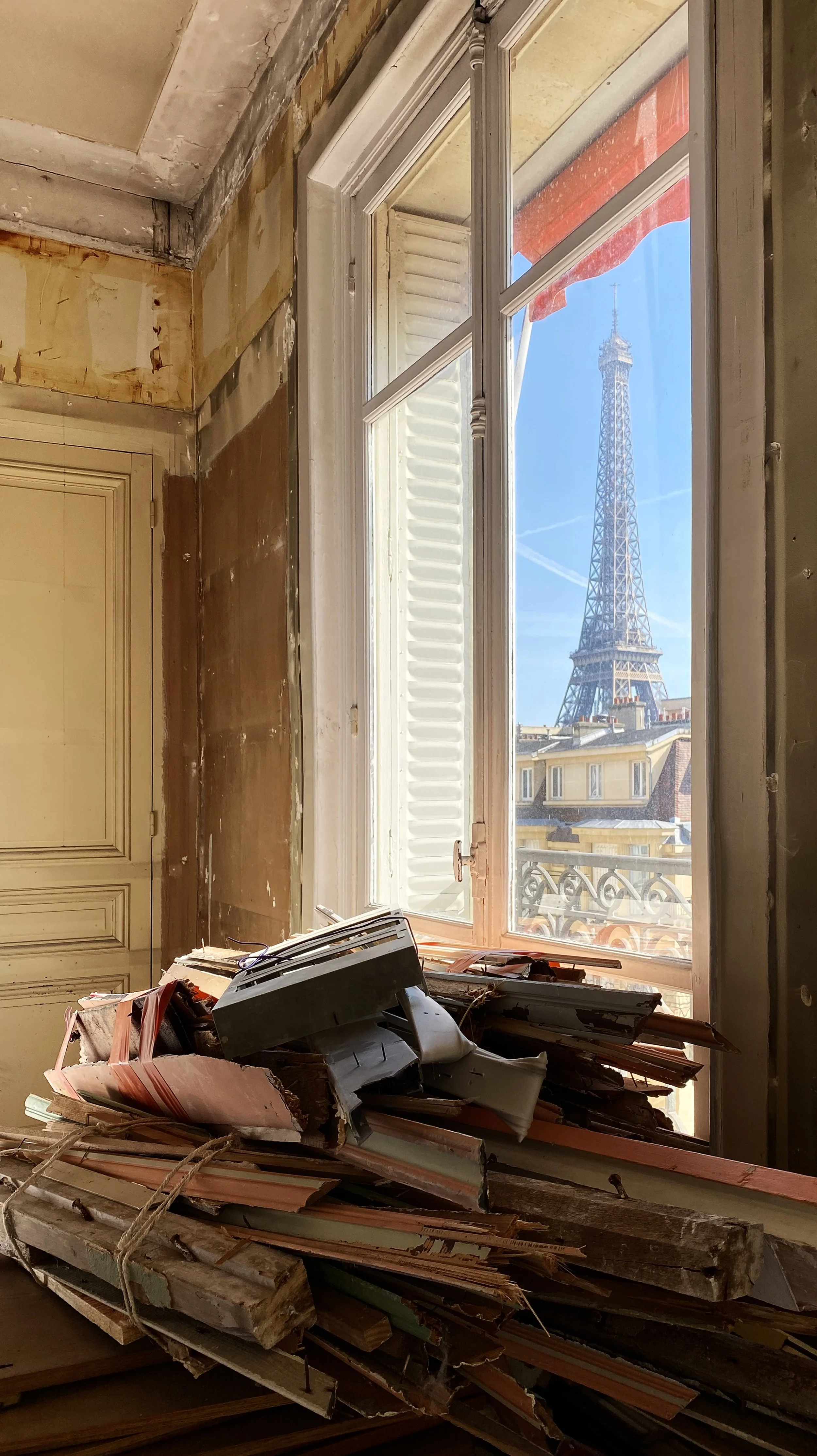 An interior room with an open window showing the Eiffel Tower in Paris, France, with construction debris and wooden planks on the floor.