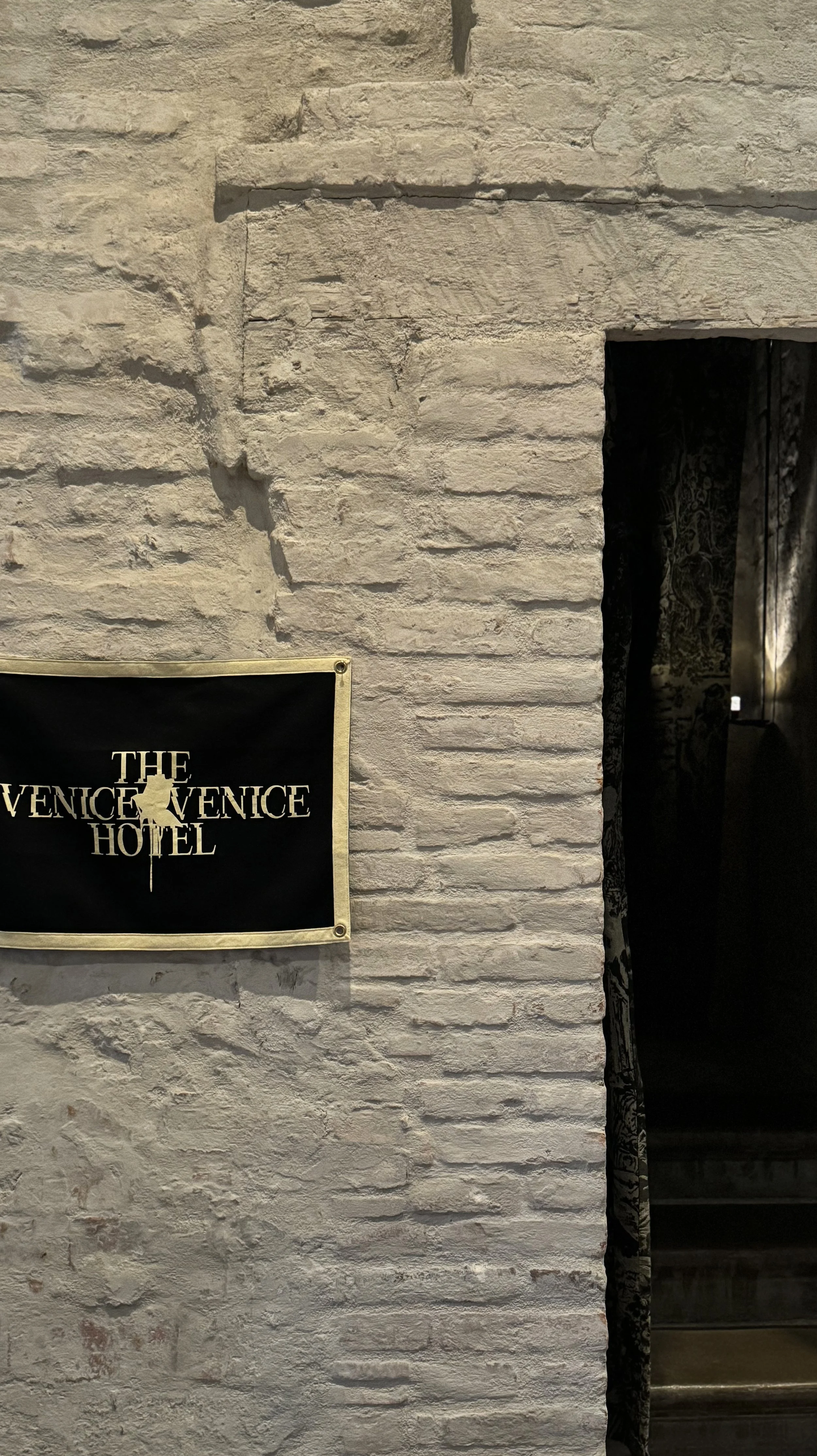 A brick wall with a black and yellow sign that reads 'The Venice Venice Hotel' partially obscured.