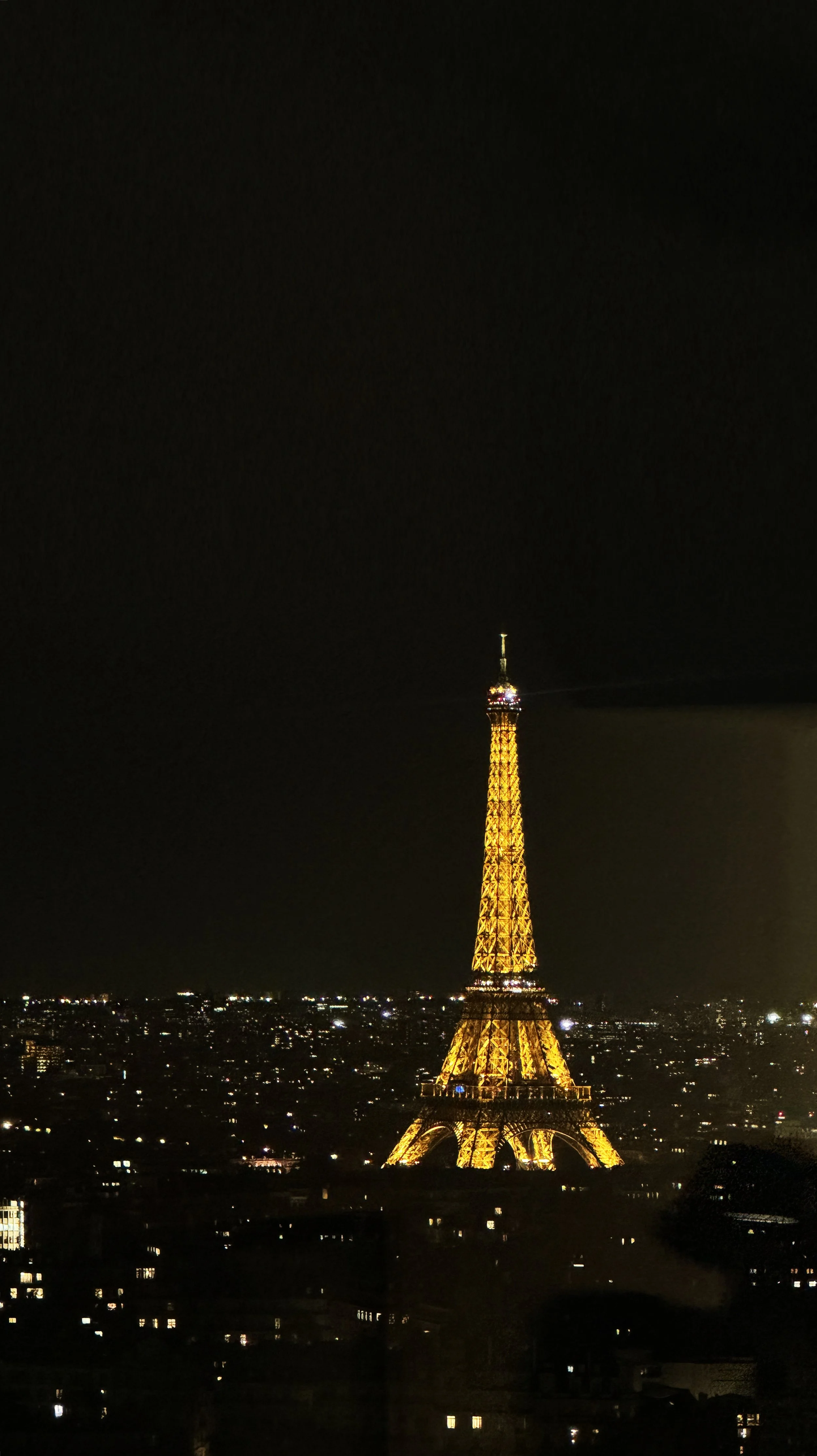 Benjamin Liatoud designs bespoke luxury architecture worldwide. Nighttime view of the Eiffel Tower illuminated in golden lights in Paris, France, with a dark sky and city lights in the background.