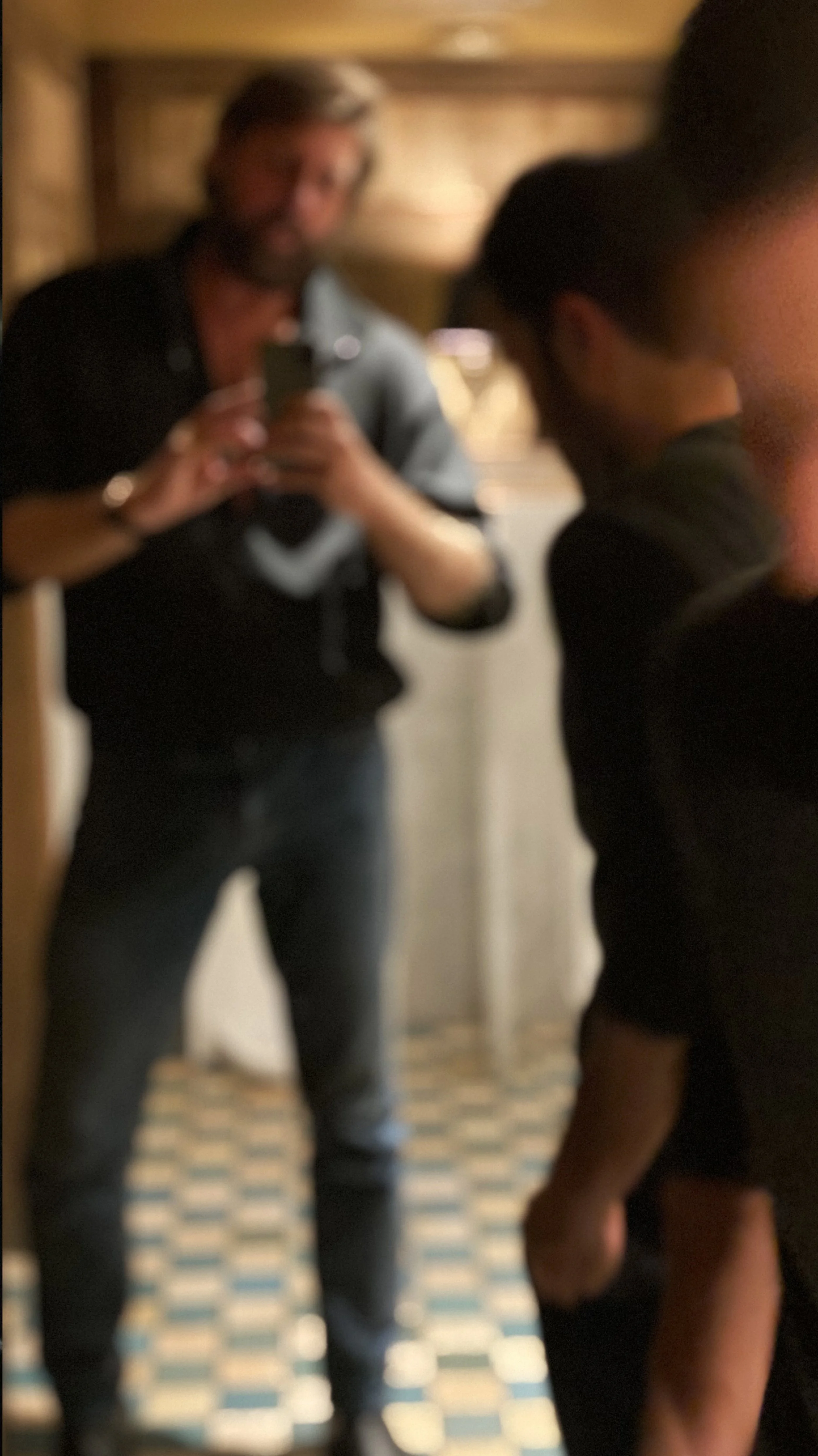 A man is taking a photo of a woman in a mirror, with other people in the background.
